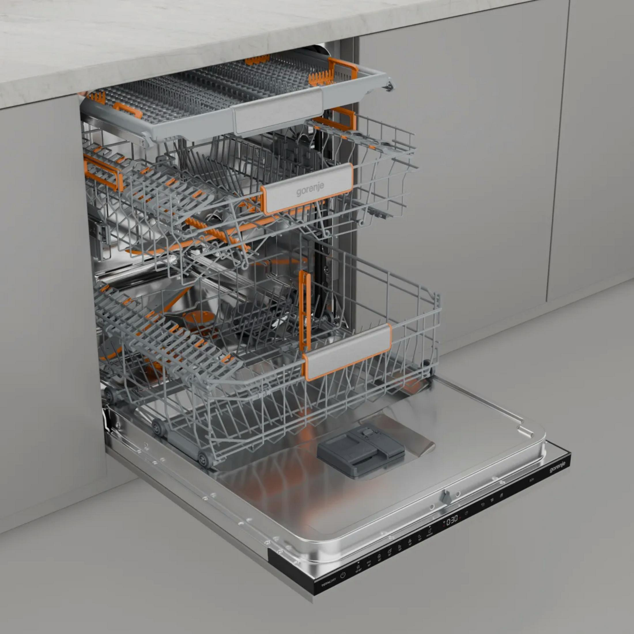Otwarta zmywarka. Widoczne dwa kosze. Pomarańczowe akcenty na koszach. Marka to Gorenje. Drzwi mają panel cyfrowy.