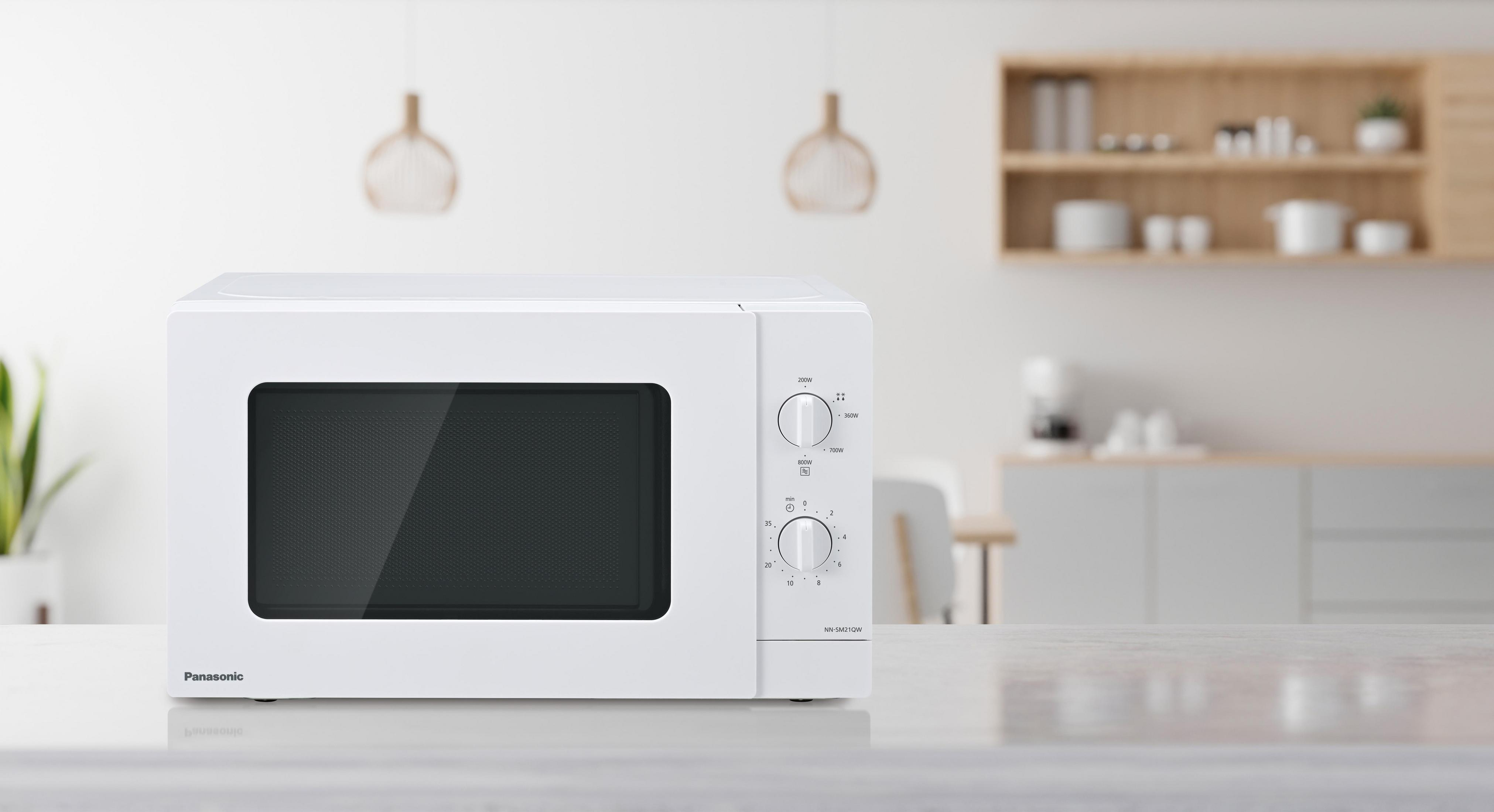 Biała kuchenka mikrofalowa Panasonic stoi na blacie. W tle rozmyta kuchnia z szafkami, stołem i lampami wiszącymi.
