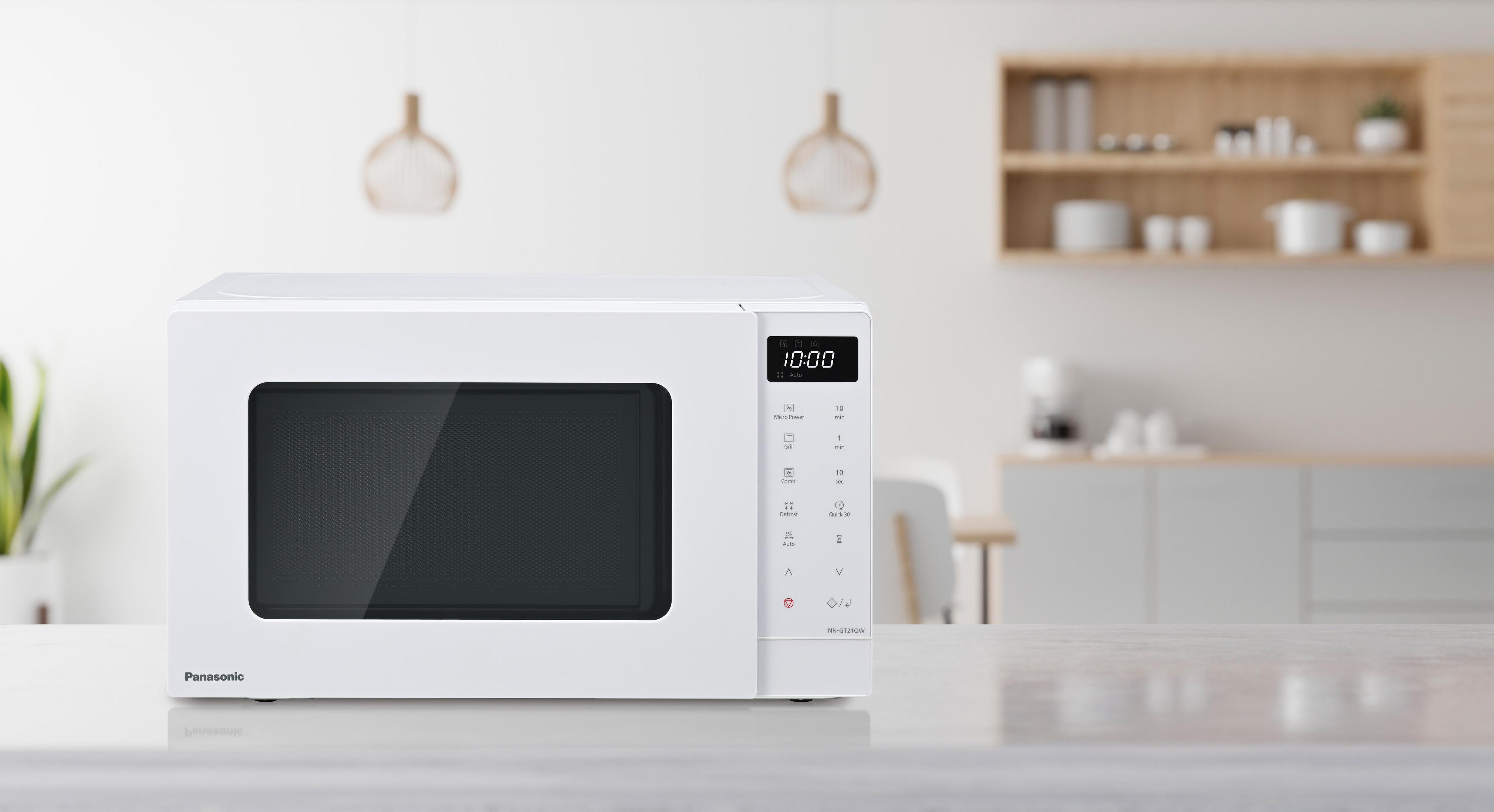 Un forno a microonde Panasonic bianco è su un tavolo. L'ora 10:00 è visualizzata. Sfondo cucina con mensole e lampade a sospensione.