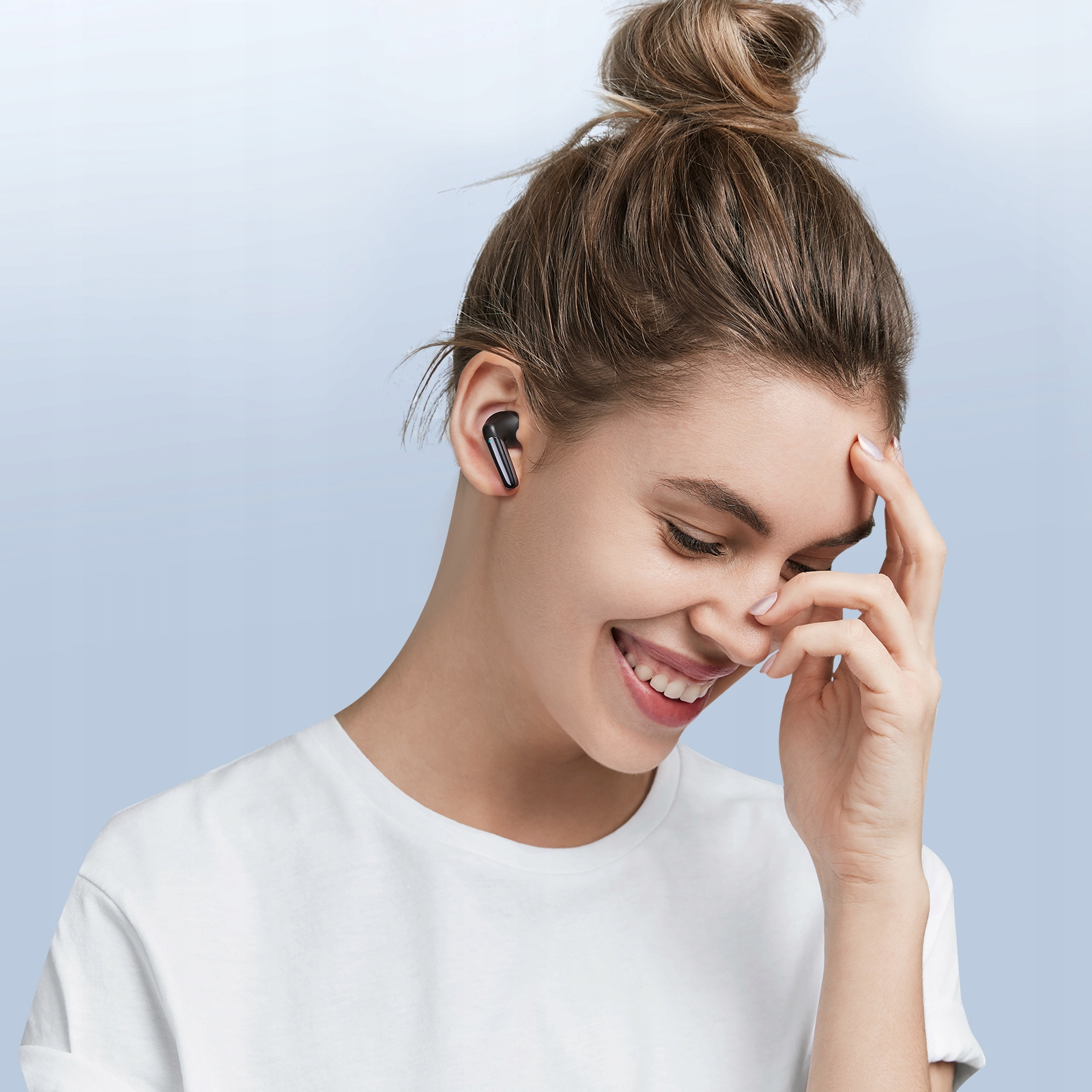 Kobieta się uśmiecha, nosząc słuchawki, dotykając czoła. Ma kok i białą koszulę na niebieskim tle.