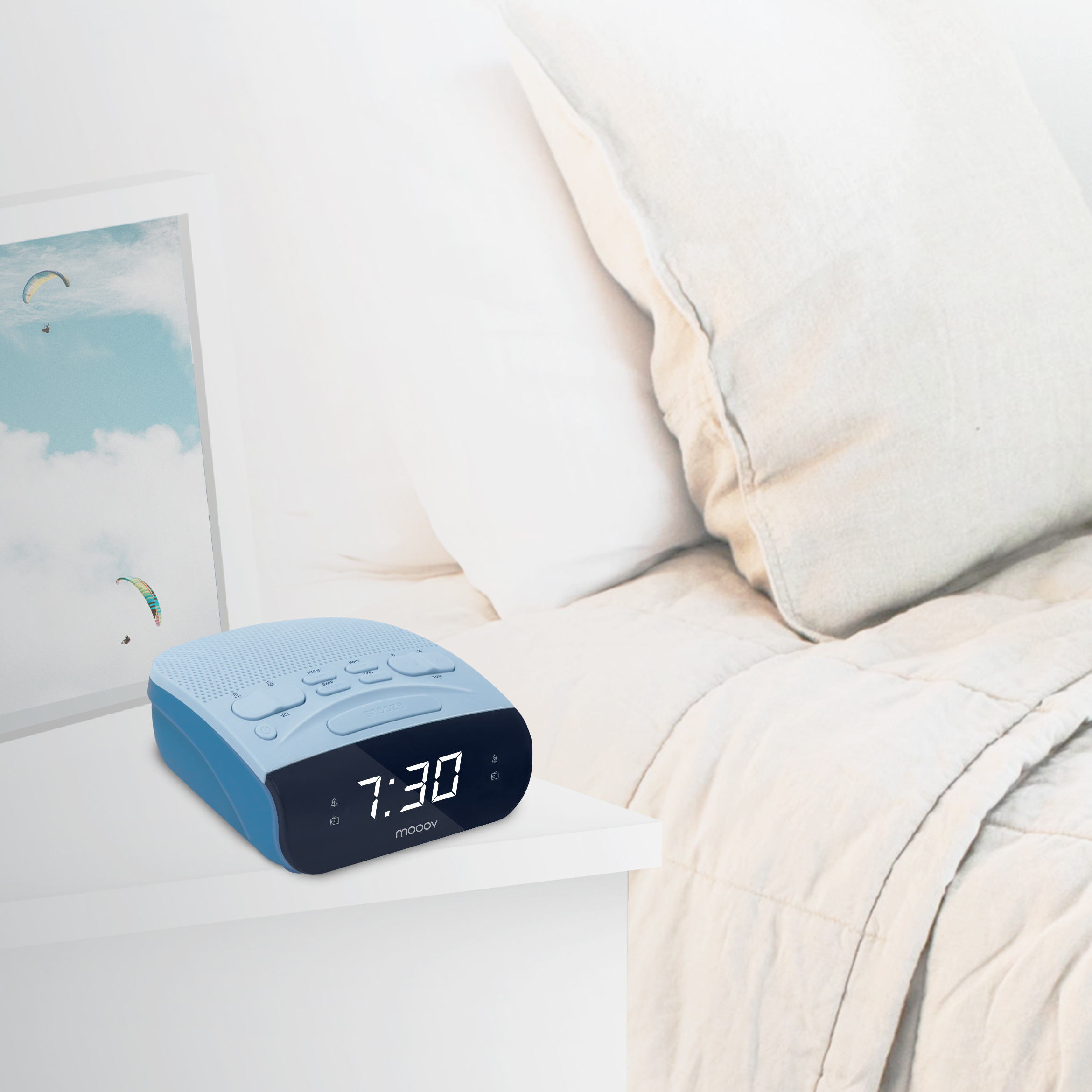 Un despertador azul y negro muestra las 7:30 en una mesita de noche blanca junto a una cama con edredón blanco.
