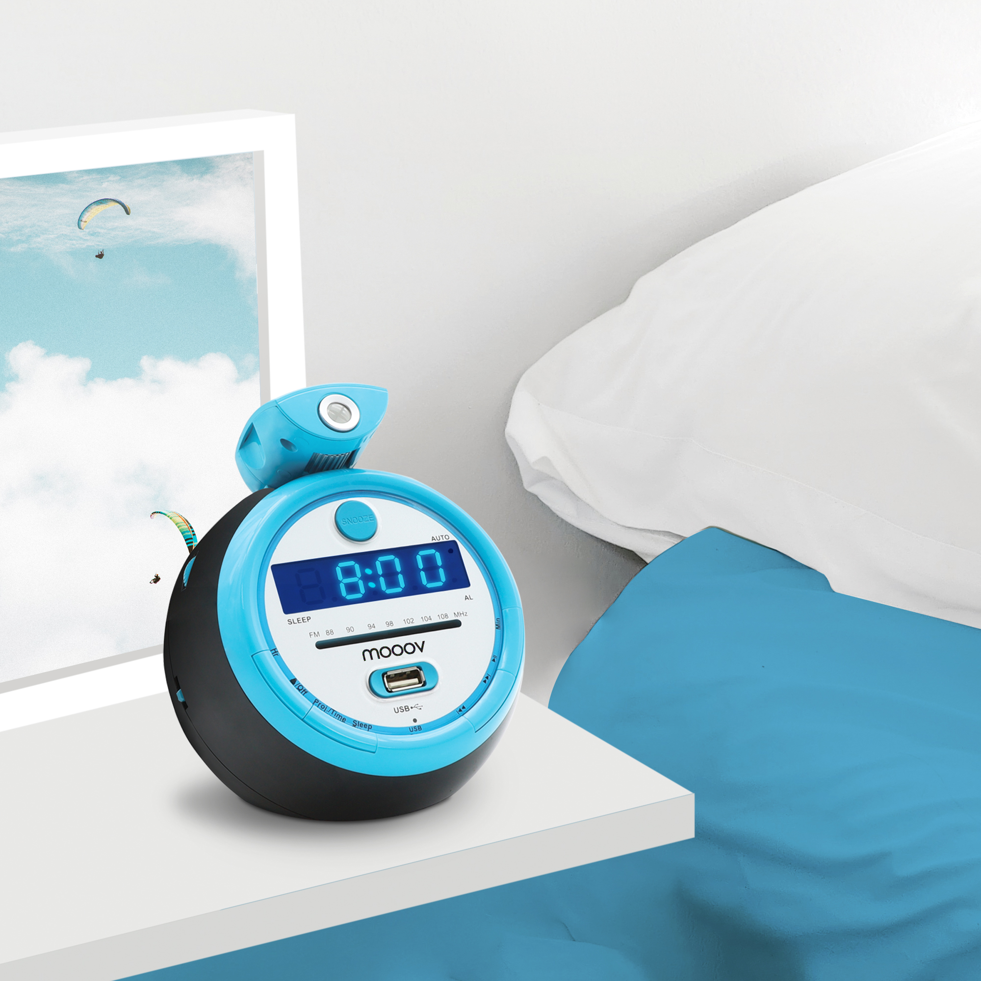 Un despertador azul y negro muestra las 8:00. Una imagen de parapentes cuelga junto al reloj. Sábanas blancas y una manta azul.
