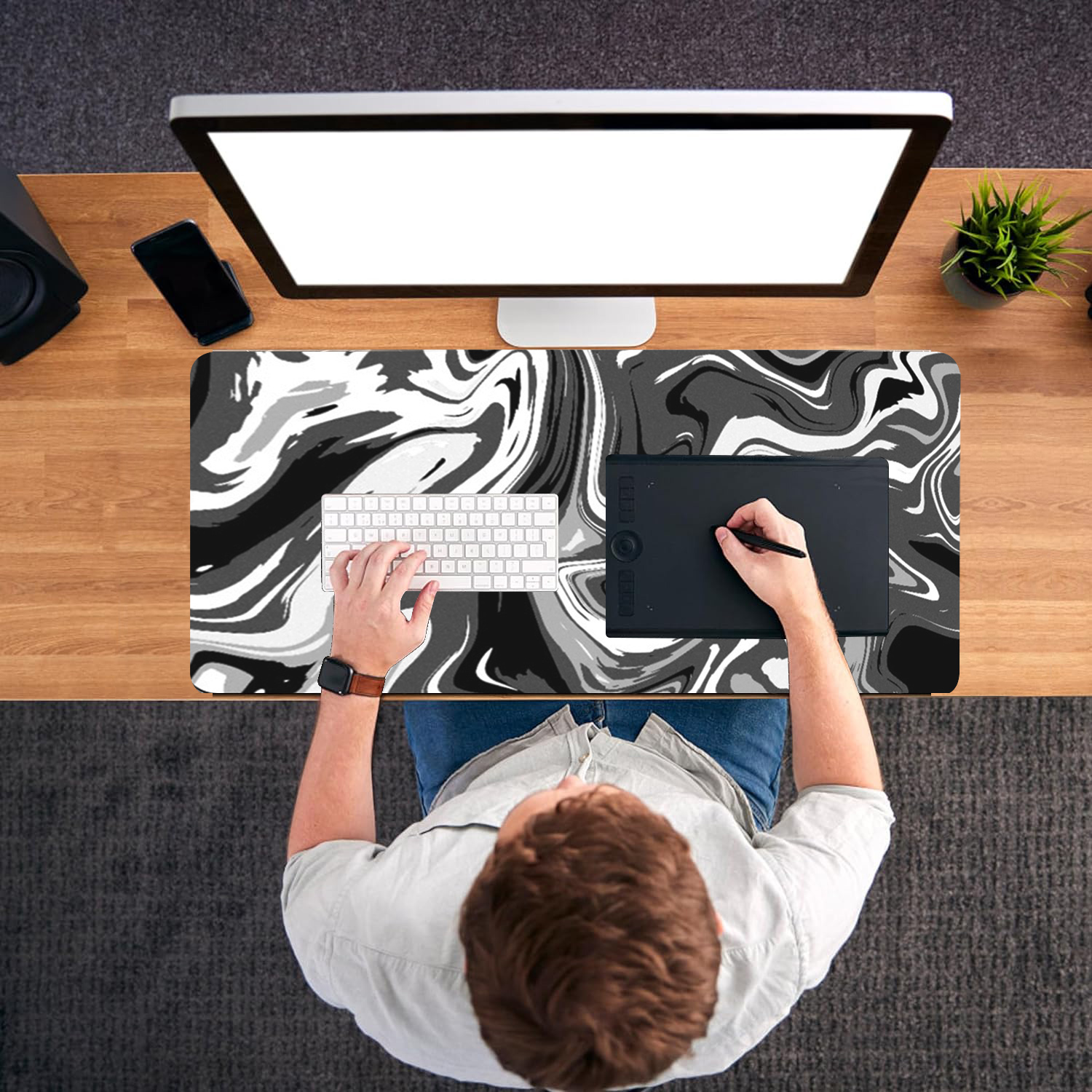 Vue de dessus d'une personne à un bureau. Elle utilise un ordinateur et une tablette graphique. Le bureau a un design noir et blanc.