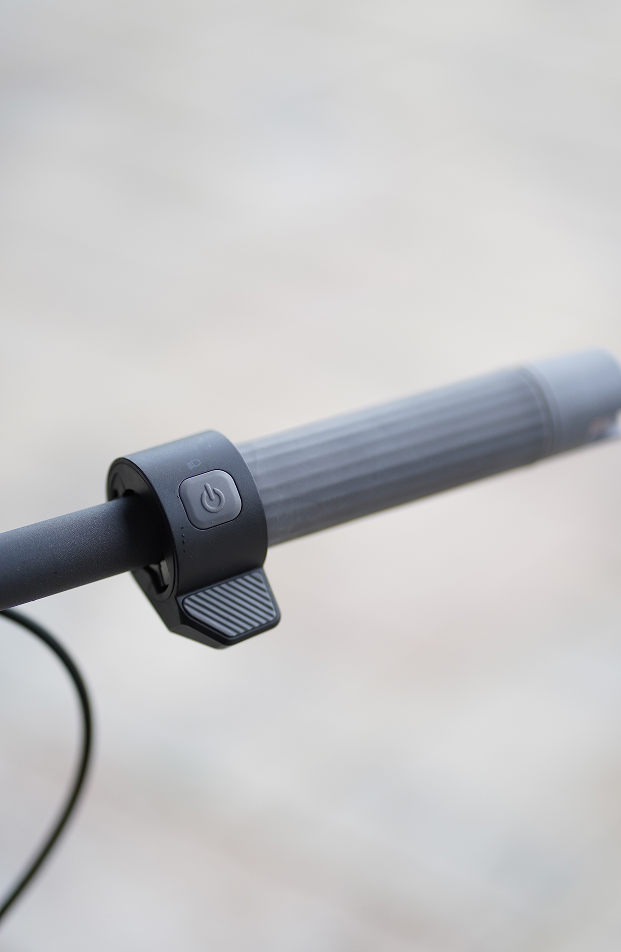Nahaufnahme eines Rollerlenkers mit Ein- und Ausschalter und strukturiertem Griff. Schwarze Bedienelemente, grauer Griff, unscharfer Hintergrund.