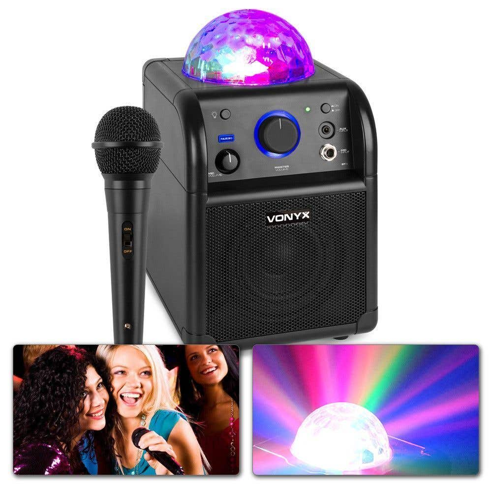 Un altoparlante nero con una palla da discoteca sopra e un microfono. Tre donne cantano in basso a sinistra. Un'altra palla da discoteca in basso a destra.