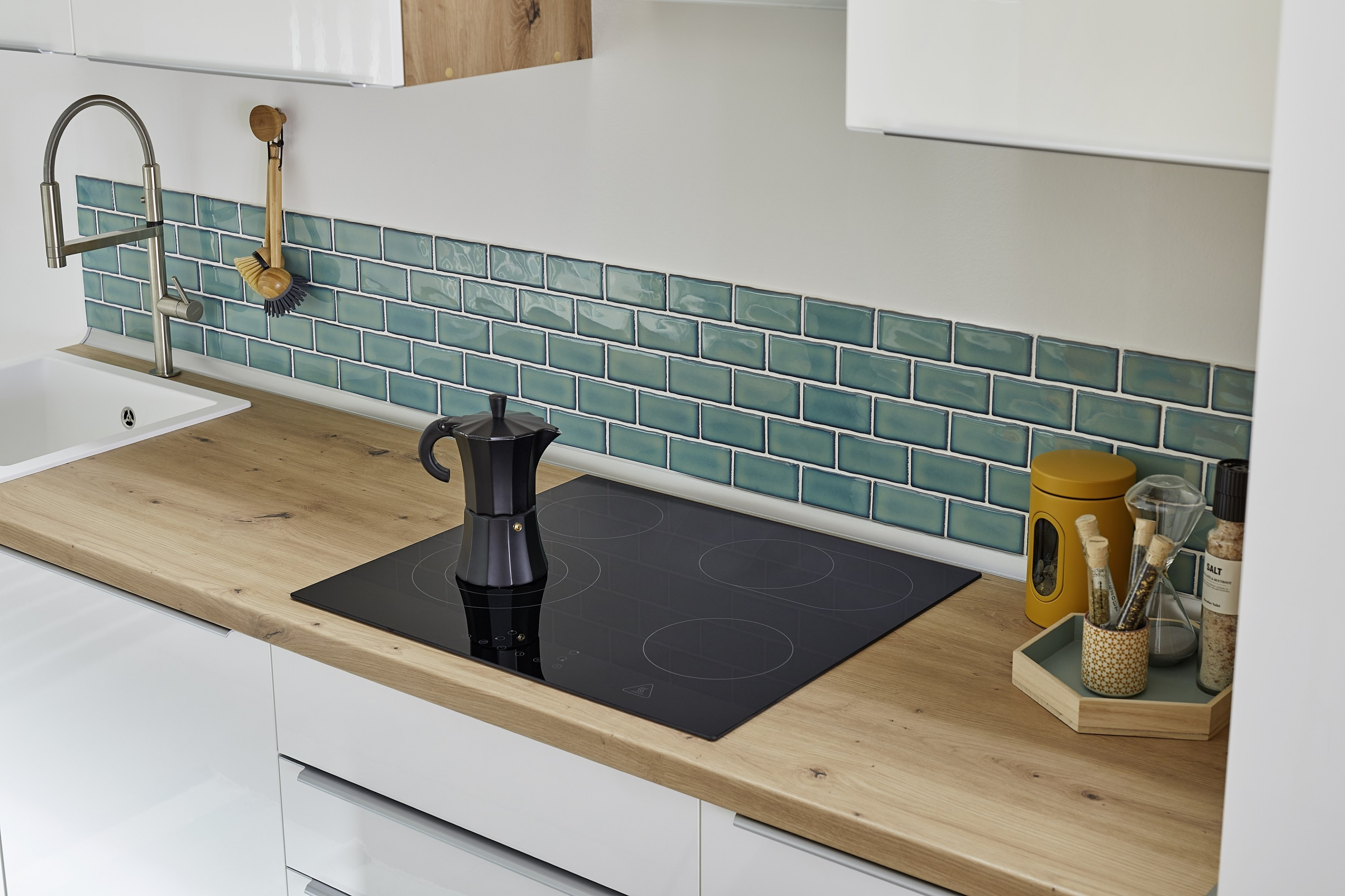 Moderne keuken met zwarte kookplaat, koffiezetapparaat en blauwe achterwand. Houten aanrecht en witte kasten.