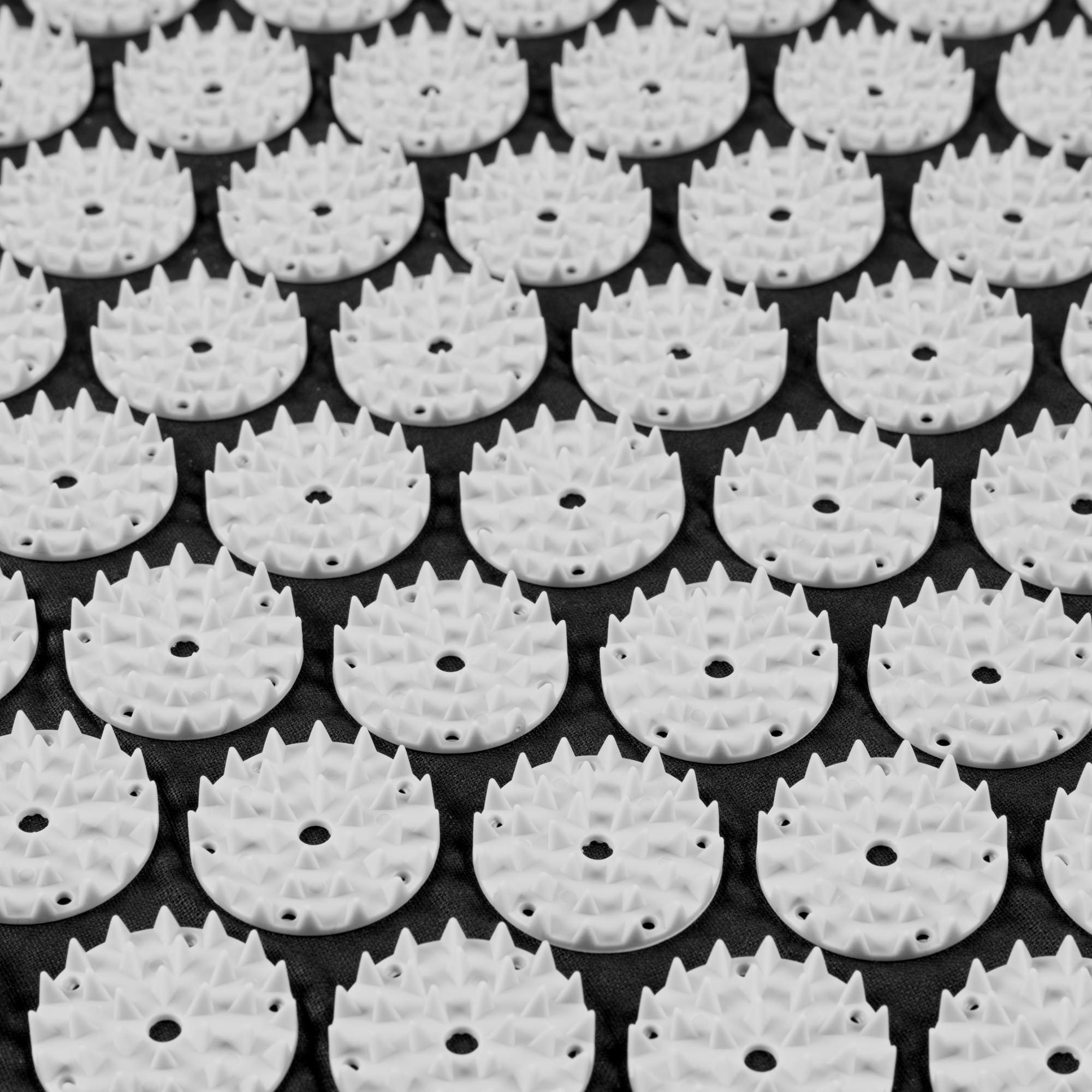 Zbliżenie maty do masażu. Białe plastikowe dyski z kolcami na ciemnej tkaninie.