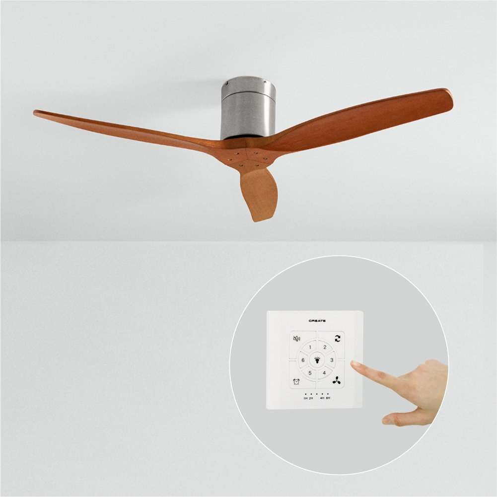 Un ventilador de techo con aspas de madera. Una mano toca un mando a distancia para el ventilador, sobre una pared blanca. El ventilador es marrón.
