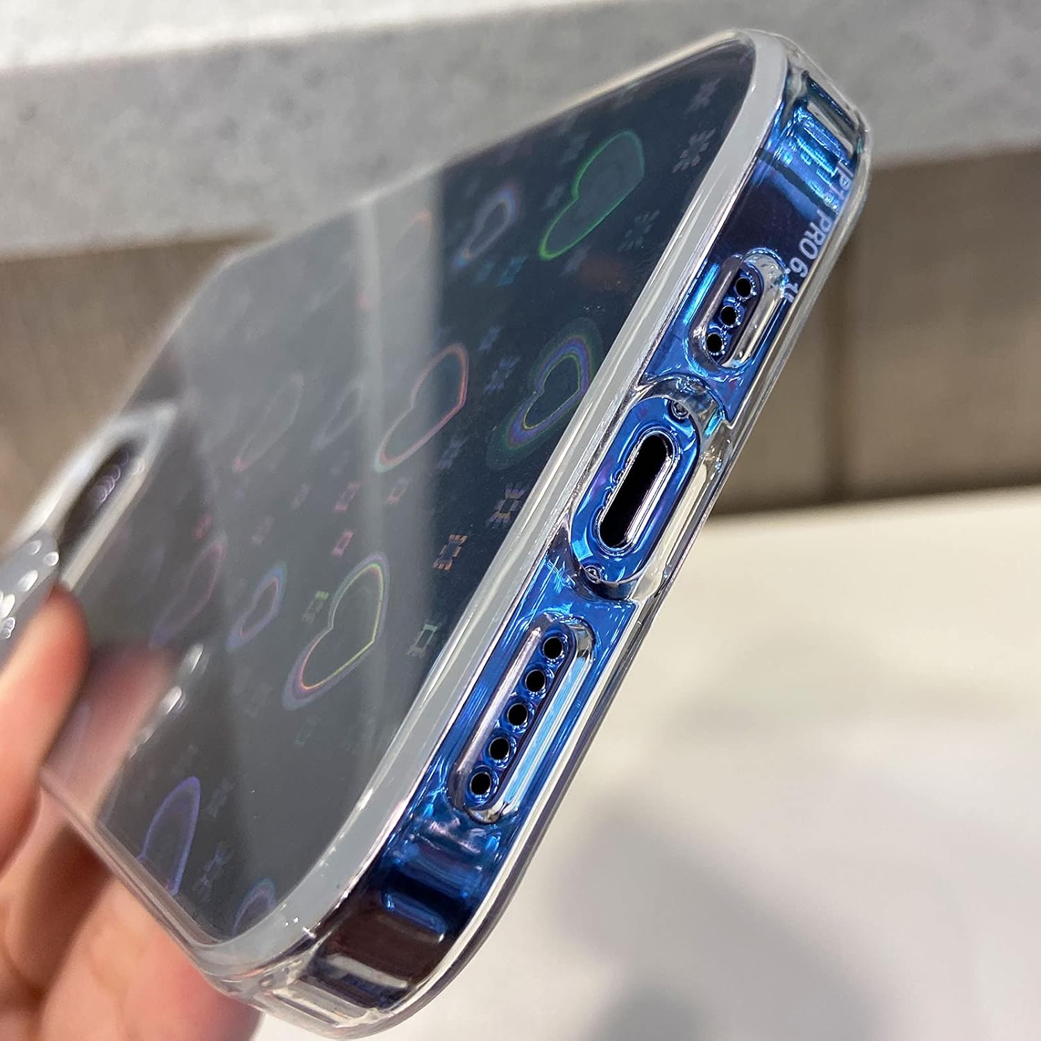 Eine transparente Handyhülle mit Herzen. Die Hülle hat einen blauen, reflektierenden Rand. Die Handyhülle wird von einer Hand gehalten.