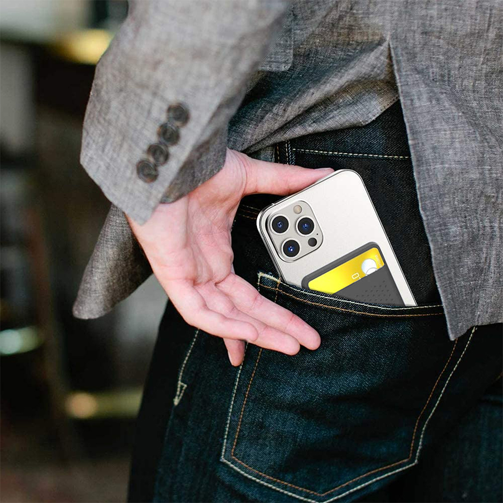 Eine Hand steckt ein Telefon mit Kartenhalter in eine Jeanstasche. Eine graue Jacke ist sichtbar.