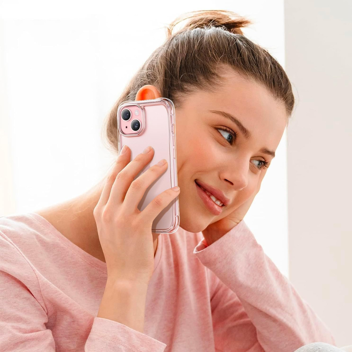 Frau hält ein rosa Telefon an ihr Ohr und lächelt. Sie trägt ein rosa Hemd und hat ihr Haar hochgesteckt. Der Hintergrund ist hell.