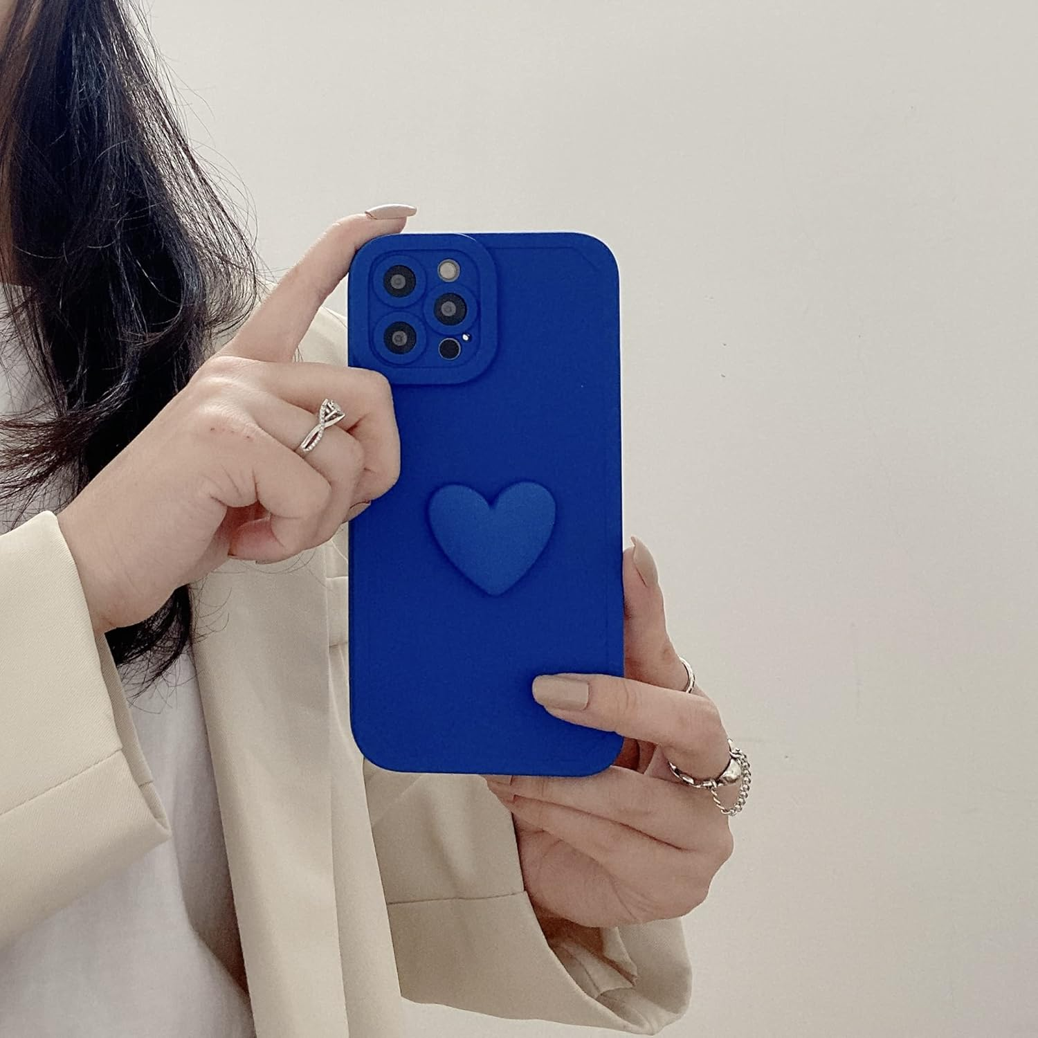 Eine Person hält eine blaue Handyhülle mit Herzdesign. Die Person trägt Ringe und eine beige Jacke. Weißer Hintergrund.