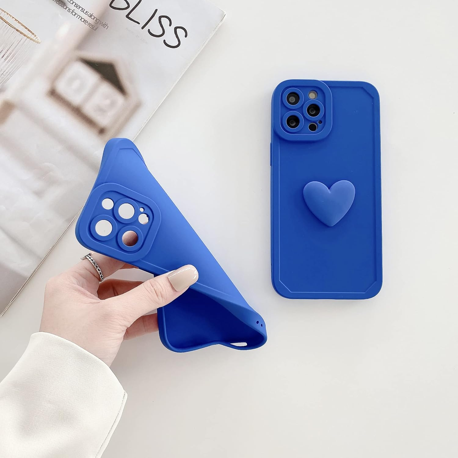 Zwei blaue Handyhüllen, eine in der Hand, die andere mit einem Herz. Im Hintergrund ein Magazin.
