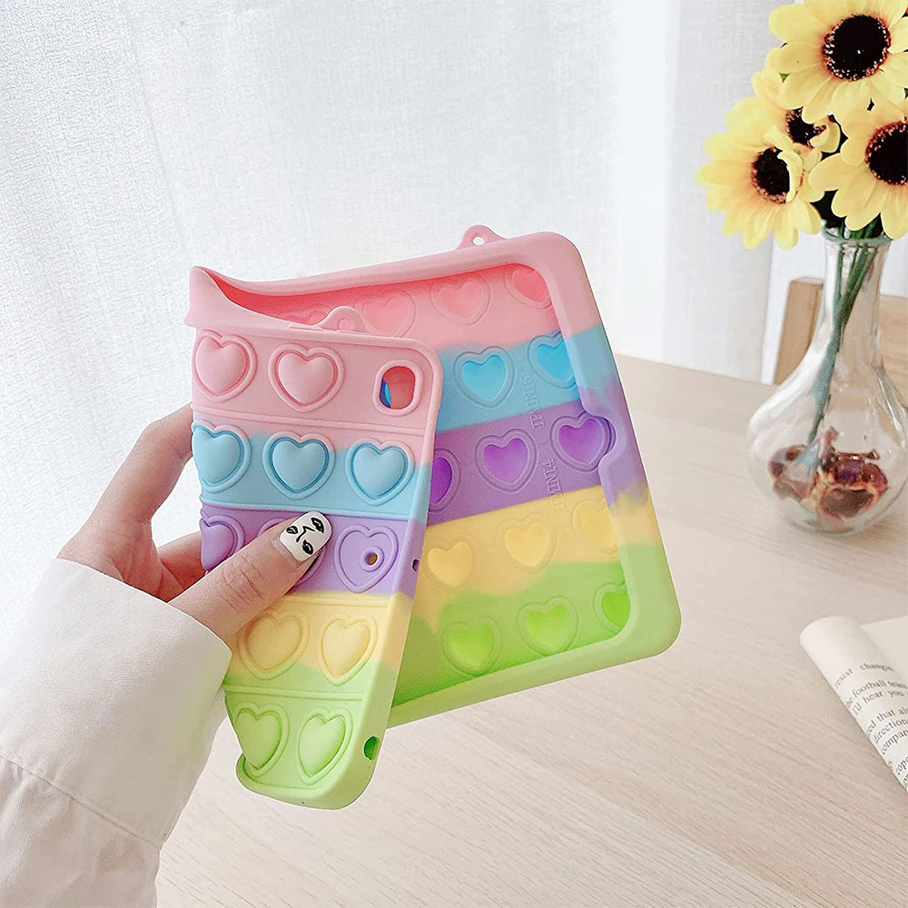 Eine Person hält eine Regenbogen-Handyhülle mit Herzformen. Sonnenblumen in einer Vase sind im Hintergrund auf einem Holztisch.