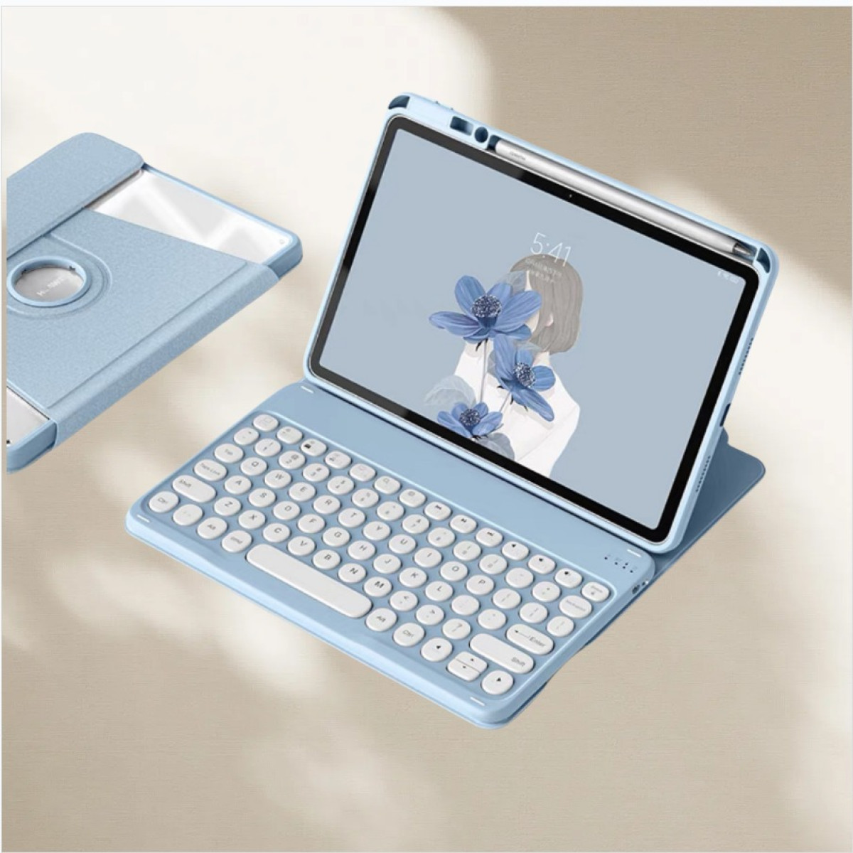 Ein blaues Tablet mit Tastatur ist geöffnet und zeigt eine Blumenillustration. Links befindet sich eine weitere Tablet-Hülle. Auf dem Tablet liegt ein Stift.