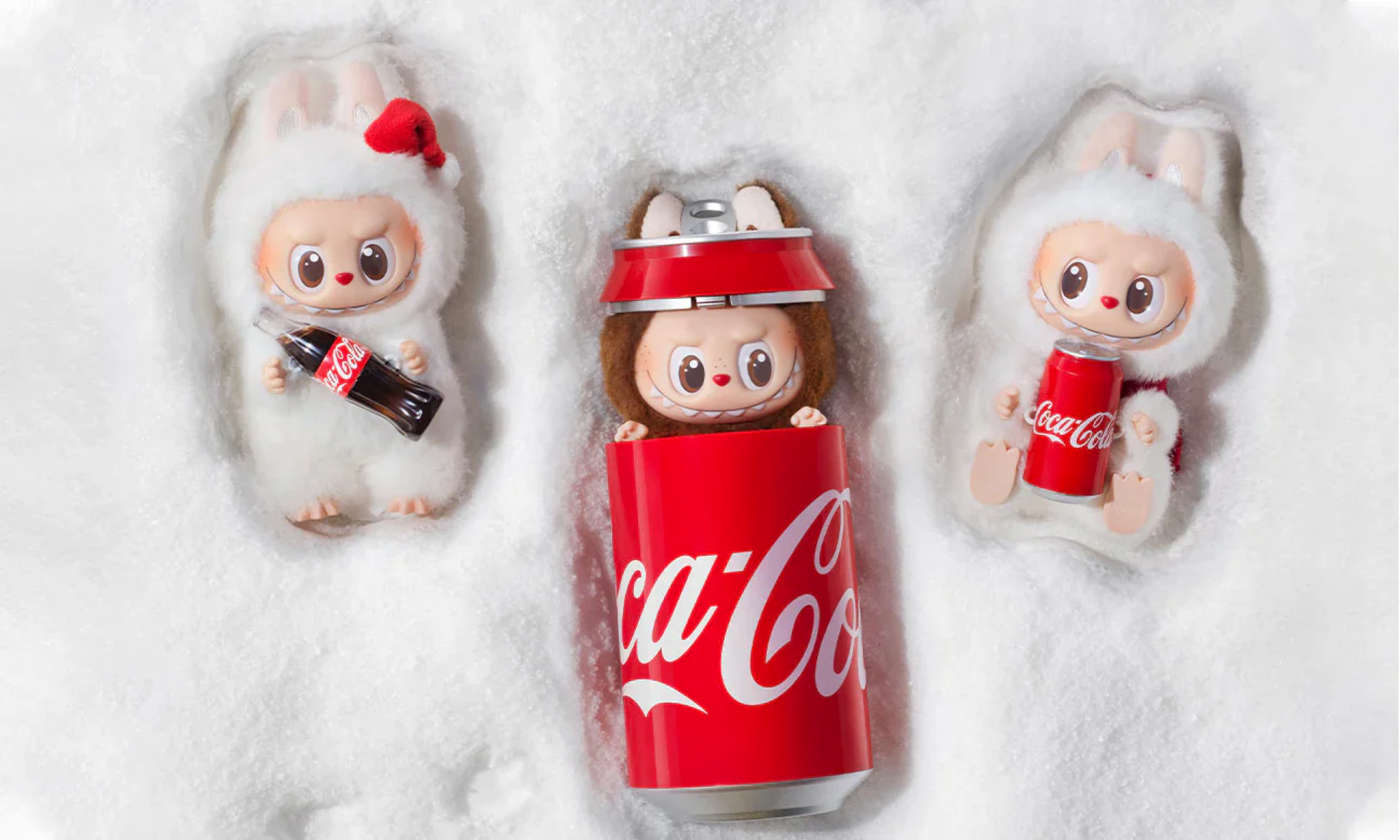Drei Zeichentrickfiguren im Schnee. Einer in einer Coca-Cola-Dose, andere halten Coca-Cola-Flaschen/Dosen. Weißes Fell und rote Akzente.