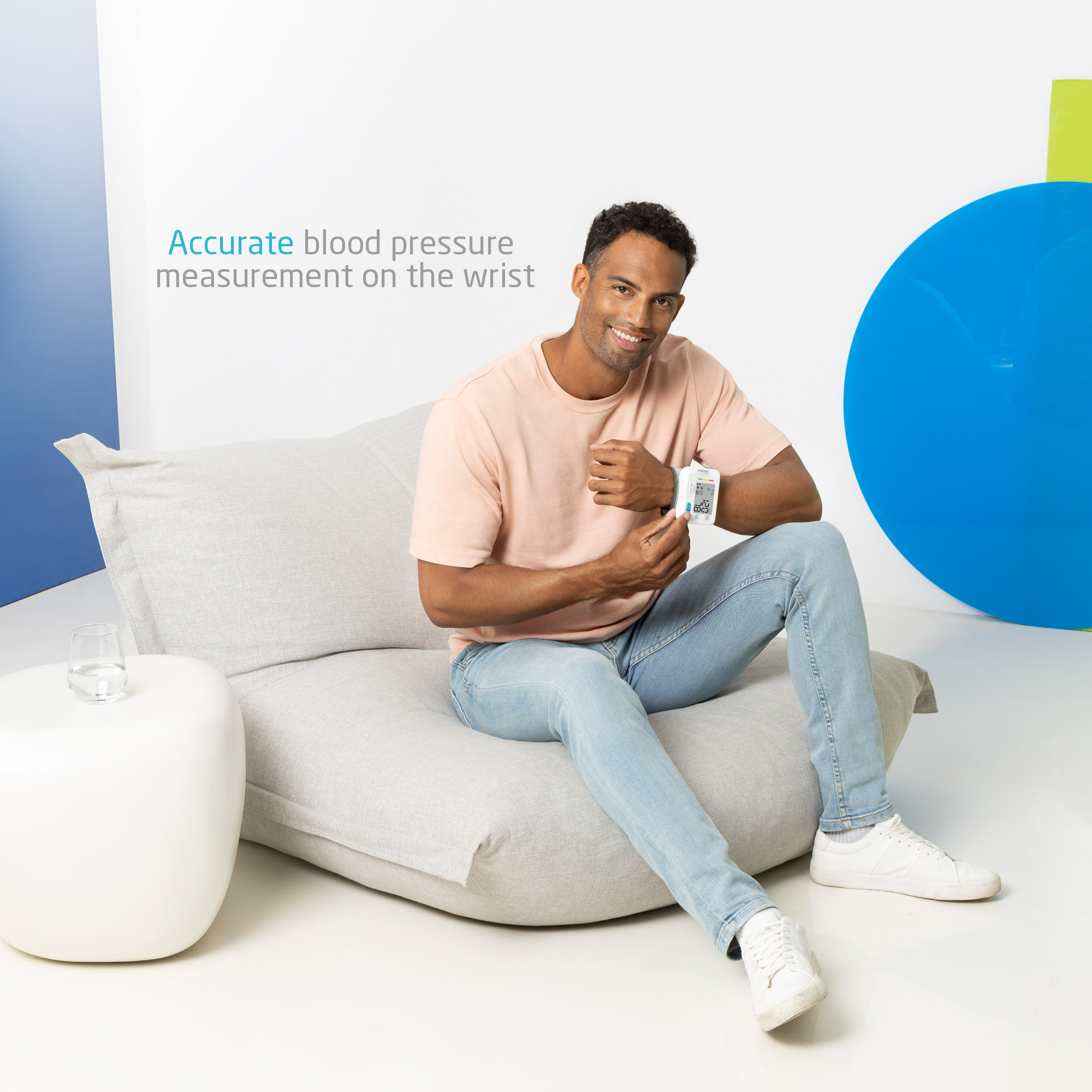 Mężczyzna siedzi na kanapie, sprawdzając ciśnienie krwi za pomocą monitora nadgarstka. Niebieskie i zielone kształty w tle.