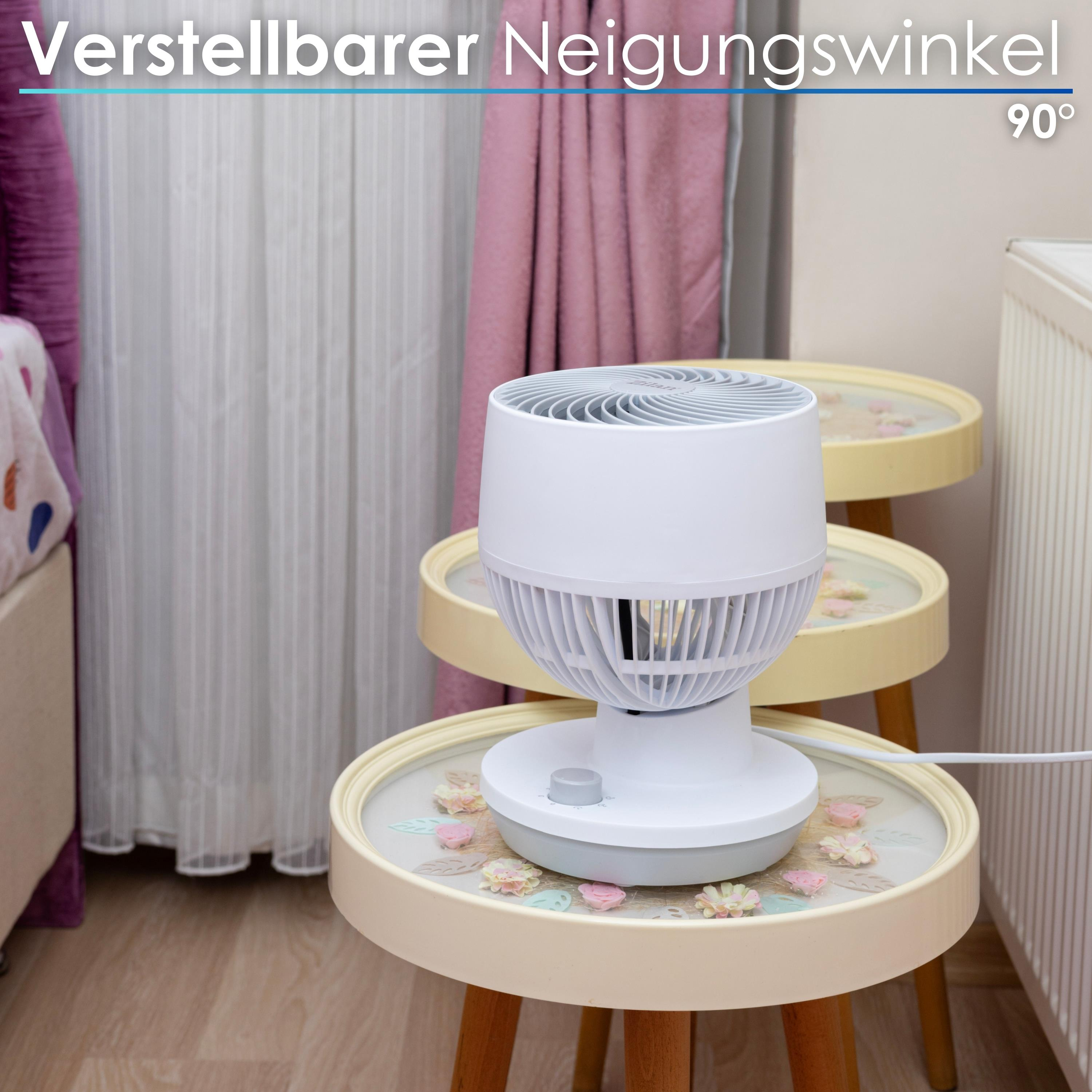 Ein weißer Ventilator steht auf einem Tisch mit Blumendekor. Vorhänge und eine Wand sind im Hintergrund.