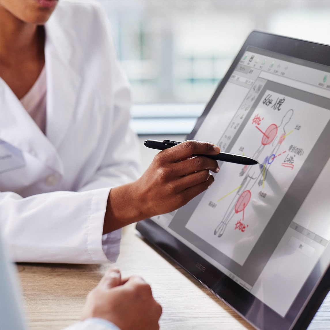 Un medico indica un diagramma anatomico su un tablet con uno stilo. Il diagramma evidenzia parti del corpo con cerchi rossi e testo giapponese.