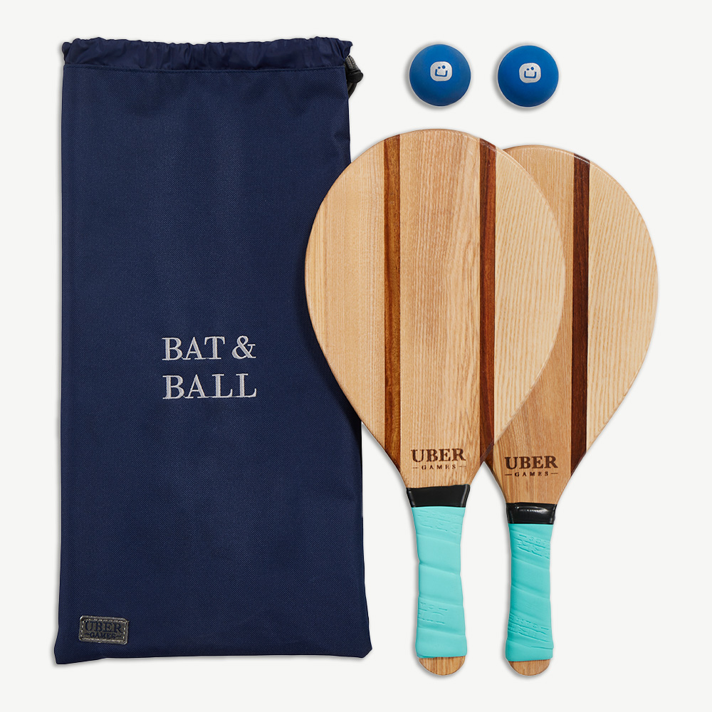 Eine marineblaue Tasche mit dem Text 'BAT & BALL', zwei Holzschläger und zwei blaue Bälle werden auf weißem Hintergrund gezeigt.