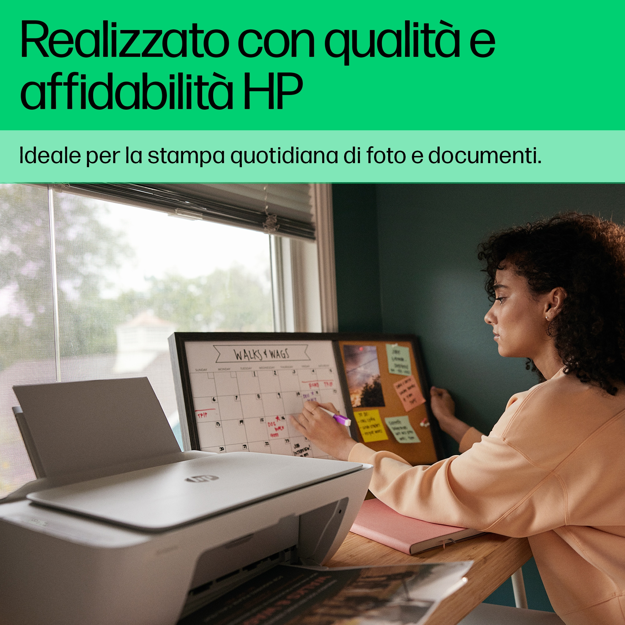 Donna che scrive su un calendario, una stampante e un blocco note su una scrivania. Lo sfondo ha una finestra e un muro verde scuro.