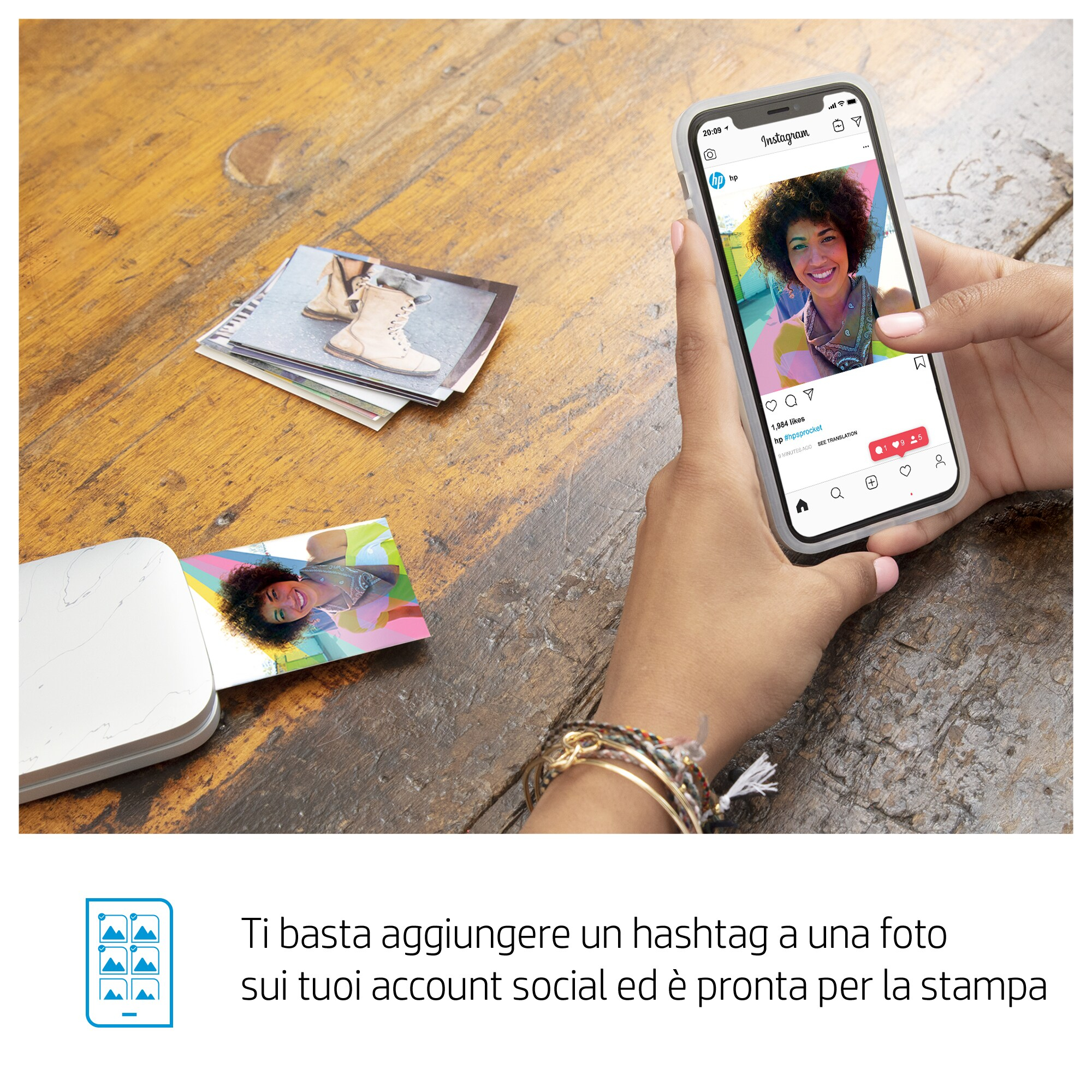 Una mujer sostiene un teléfono con una publicación de Instagram. Fotos sobre la mesa. Una impresora a la izquierda.