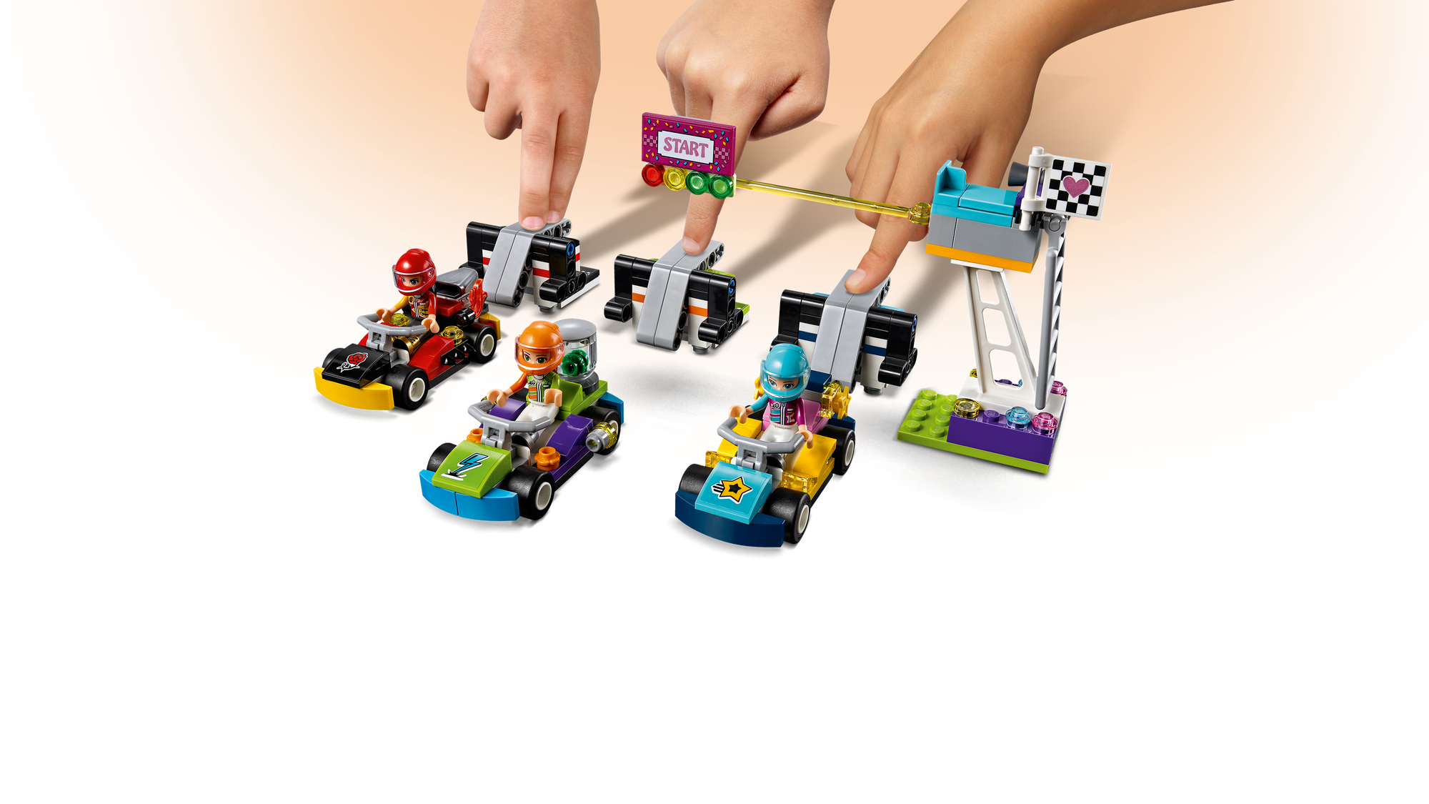 Scena di gara Lego Friends. Quattro mini-figure in go-kart sulla linea di partenza. Mani sui meccanismi di partenza.