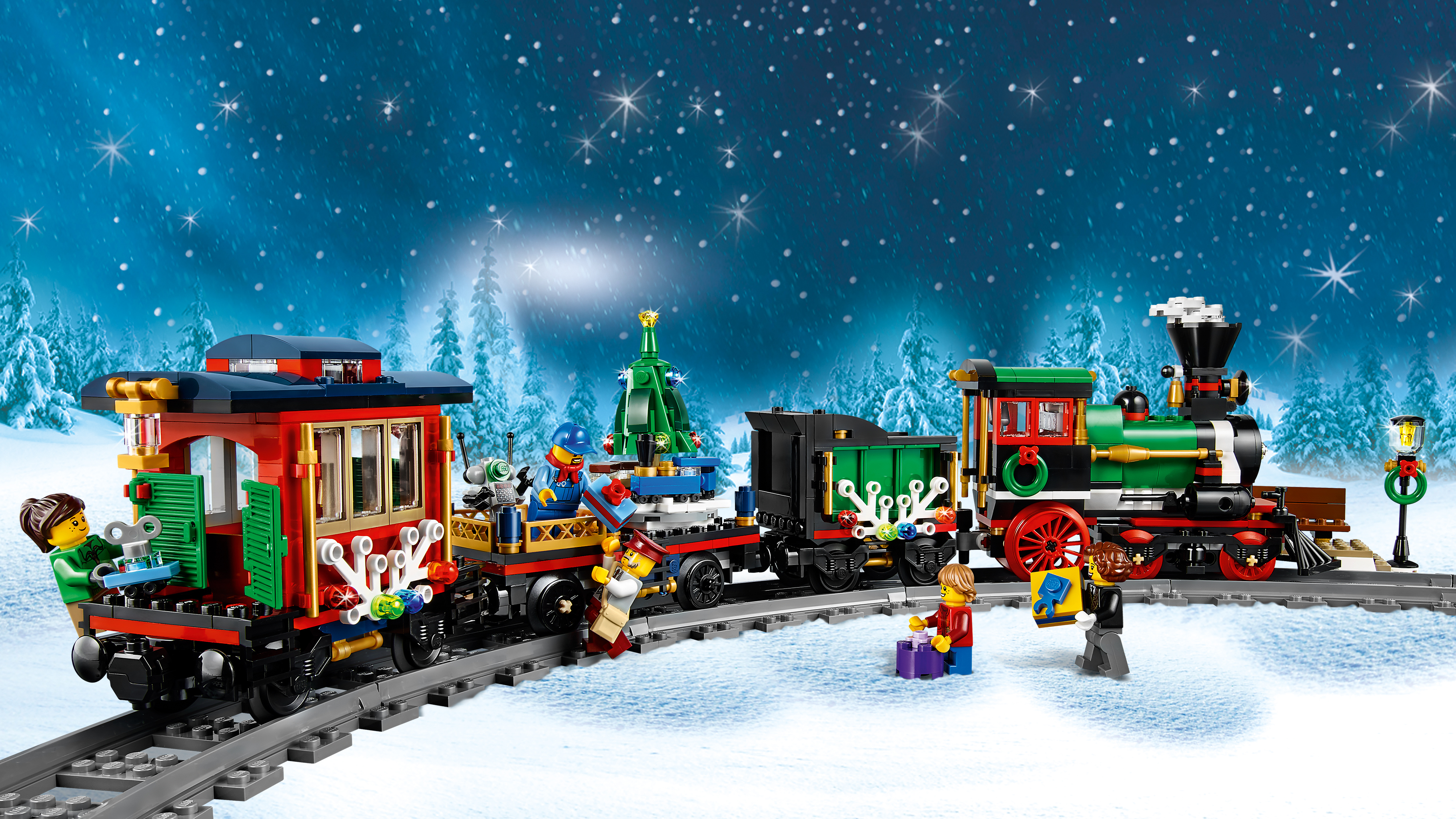 A Lego Christmas train on tracks in a snowy scene. Figures are loading gifts. Background shows snowy trees and a starry sky.