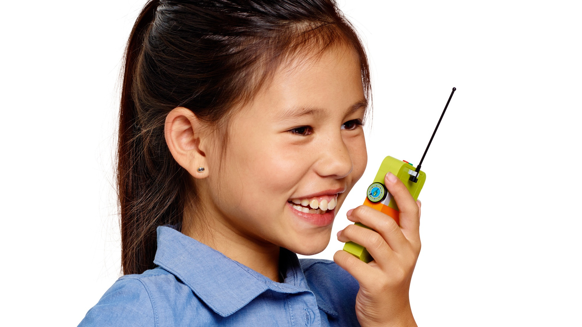 Uśmiechnięta dziewczyna z ciemnymi włosami trzyma zielone walkie-talkie. Ma na sobie niebieską koszulę i mały kolczyk.