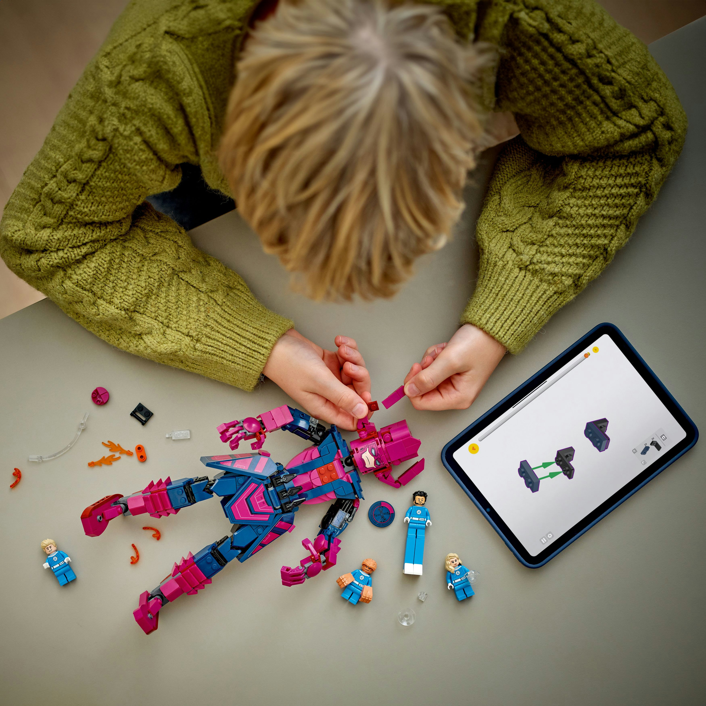 Dziecko składa figurkę Lego. Figurka to Galactus. Tablet pokazuje instrukcje. Obecnych jest kilka figurek Lego.