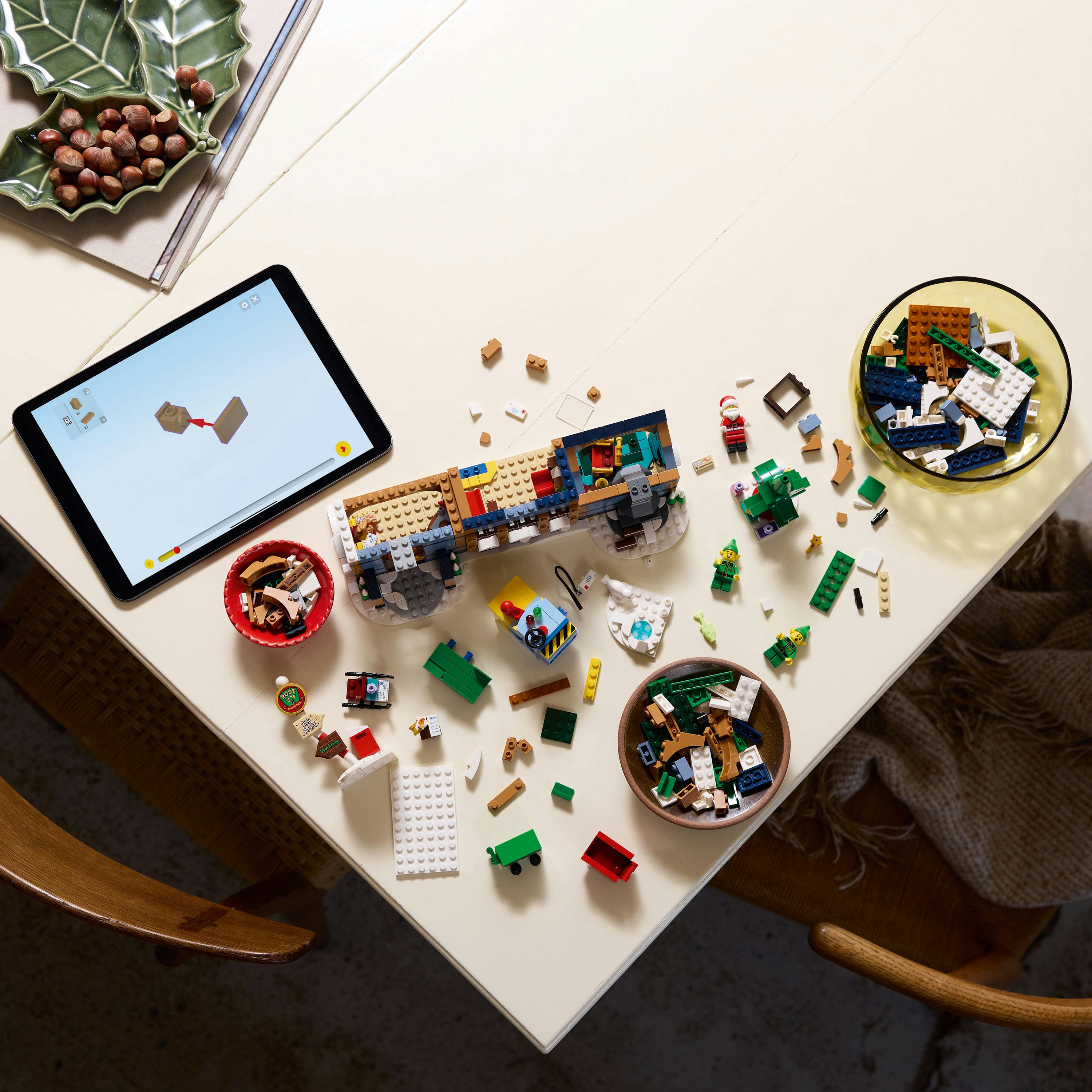 Un tavolo con un set Lego, un tablet, un piatto verde a forma di foglia con noci e vari pezzi Lego in ciotole.