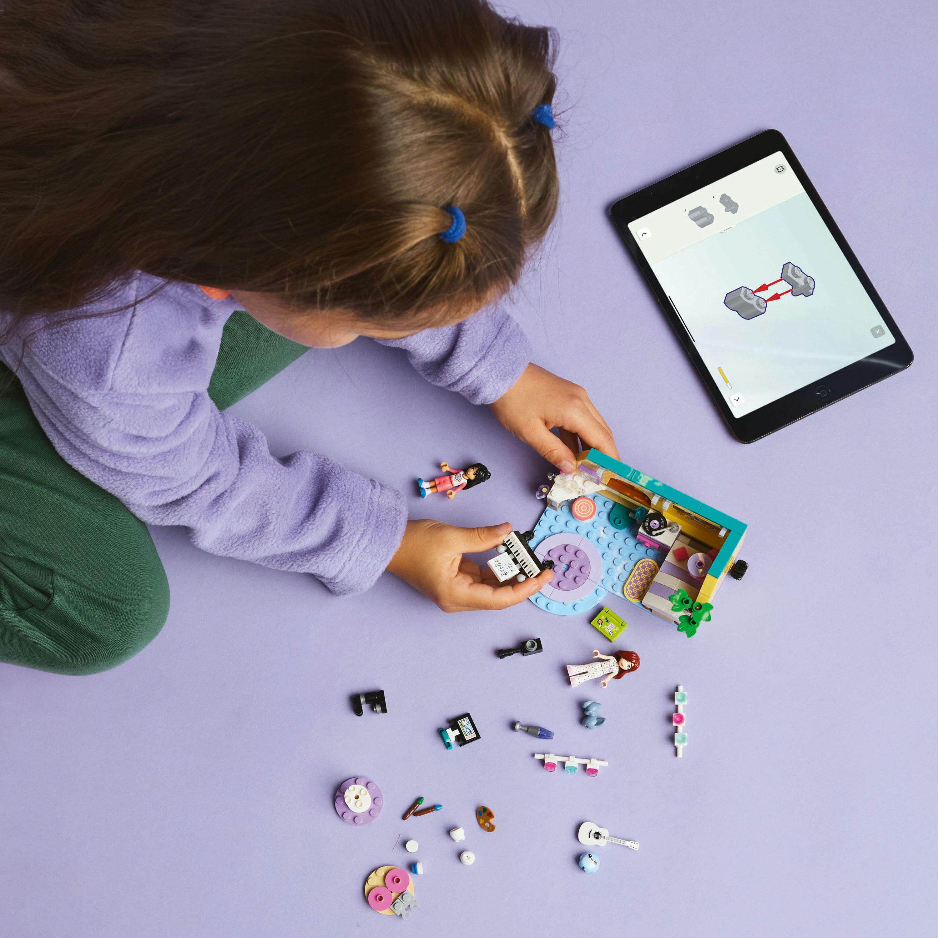Dziecko bawi się Lego, kierując się tabletem. Klocki Lego i budowla na fioletowej powierzchni.