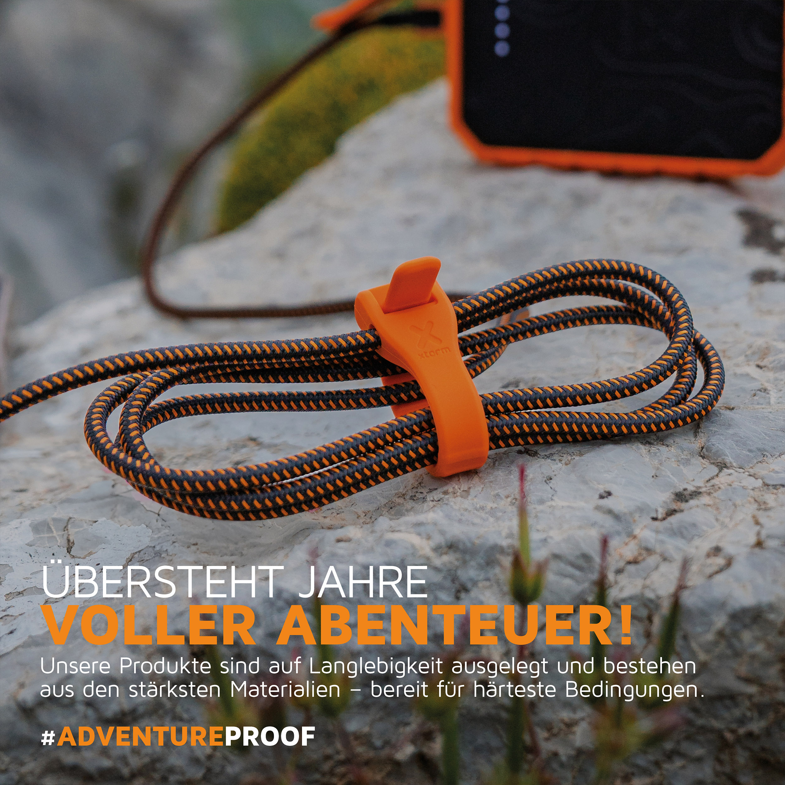 Ein orangefarbener Kabelbinder hält ein schwarz-oranges Kabel auf einem Felsen. Im Hintergrund befindet sich ein schwarz-oranges Gerät.