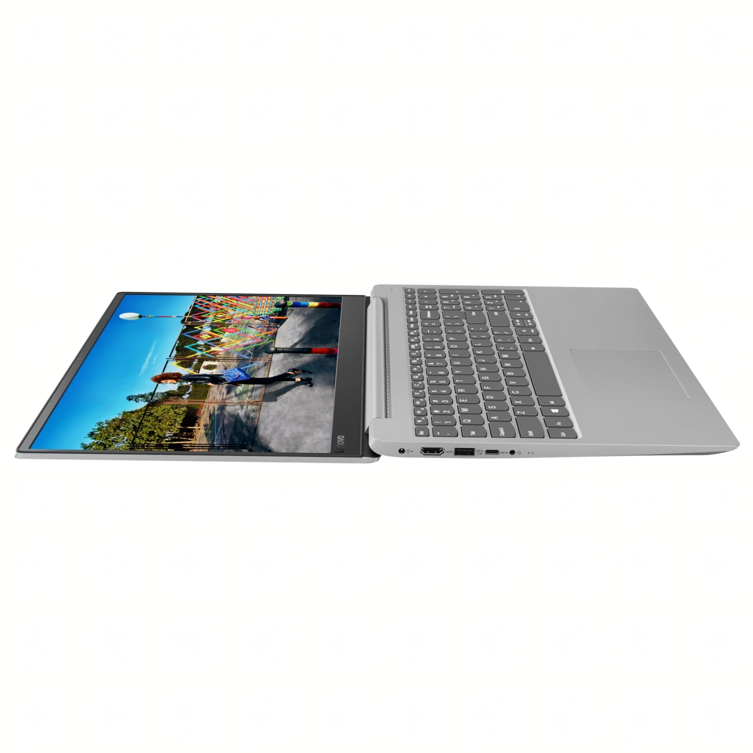 Un portátil Lenovo plateado está abierto, mostrando una pantalla con una escena de parque. El teclado es visible. El fondo es blanco.