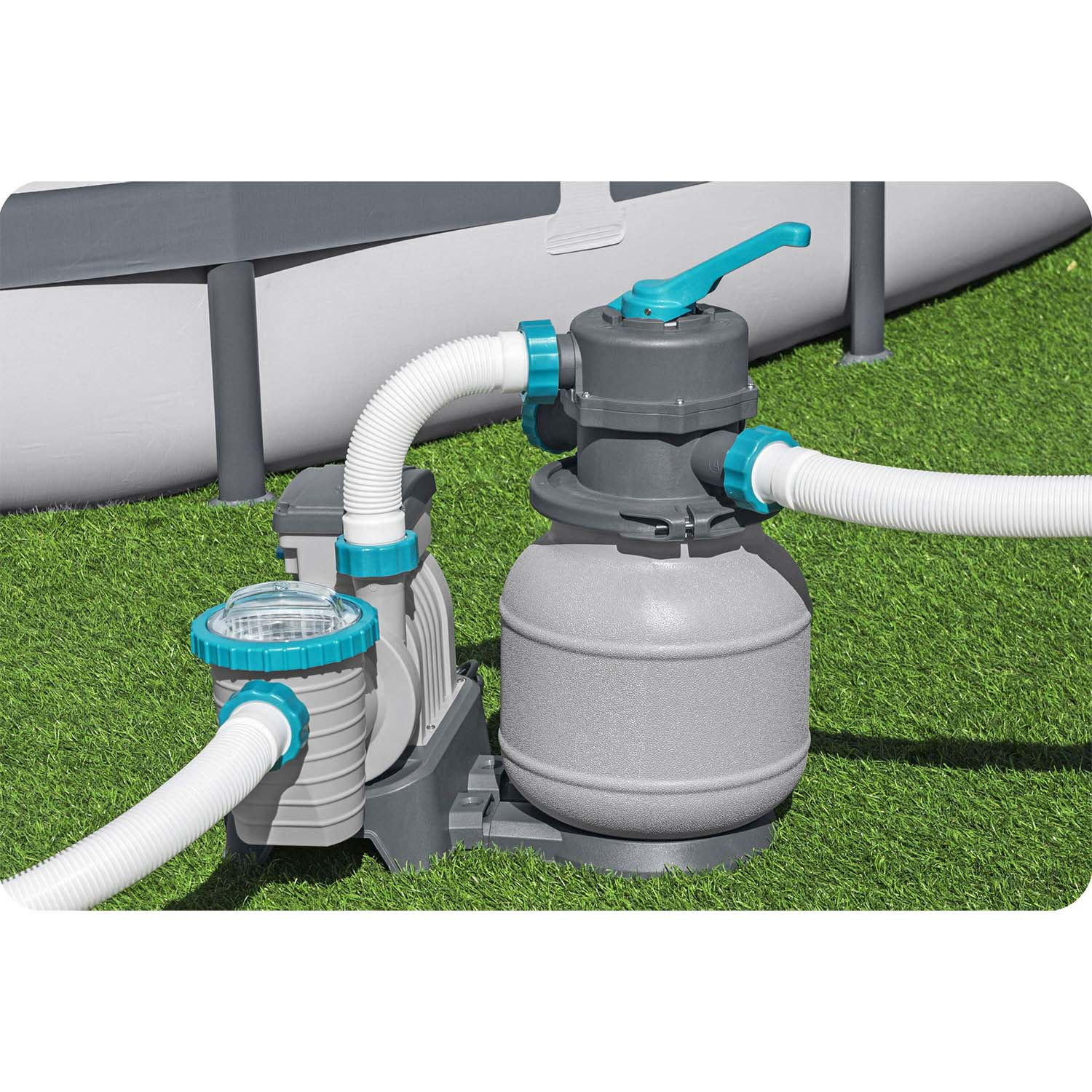 System filtracji basenowej na trawie, z wężami i szarym zbiornikiem. W tle basen.