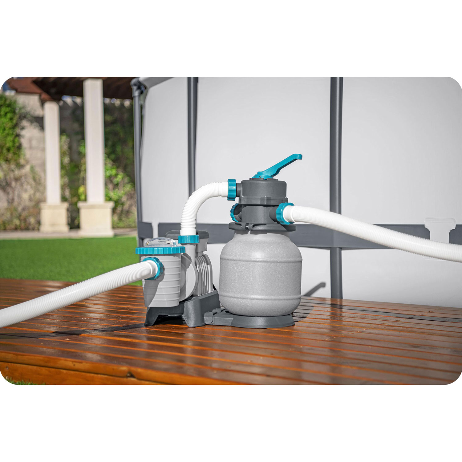 System filtracji basenu na drewnianym tarasie. System posiada szary filtr, niebieskie i białe węże oraz niebieską dźwignię.