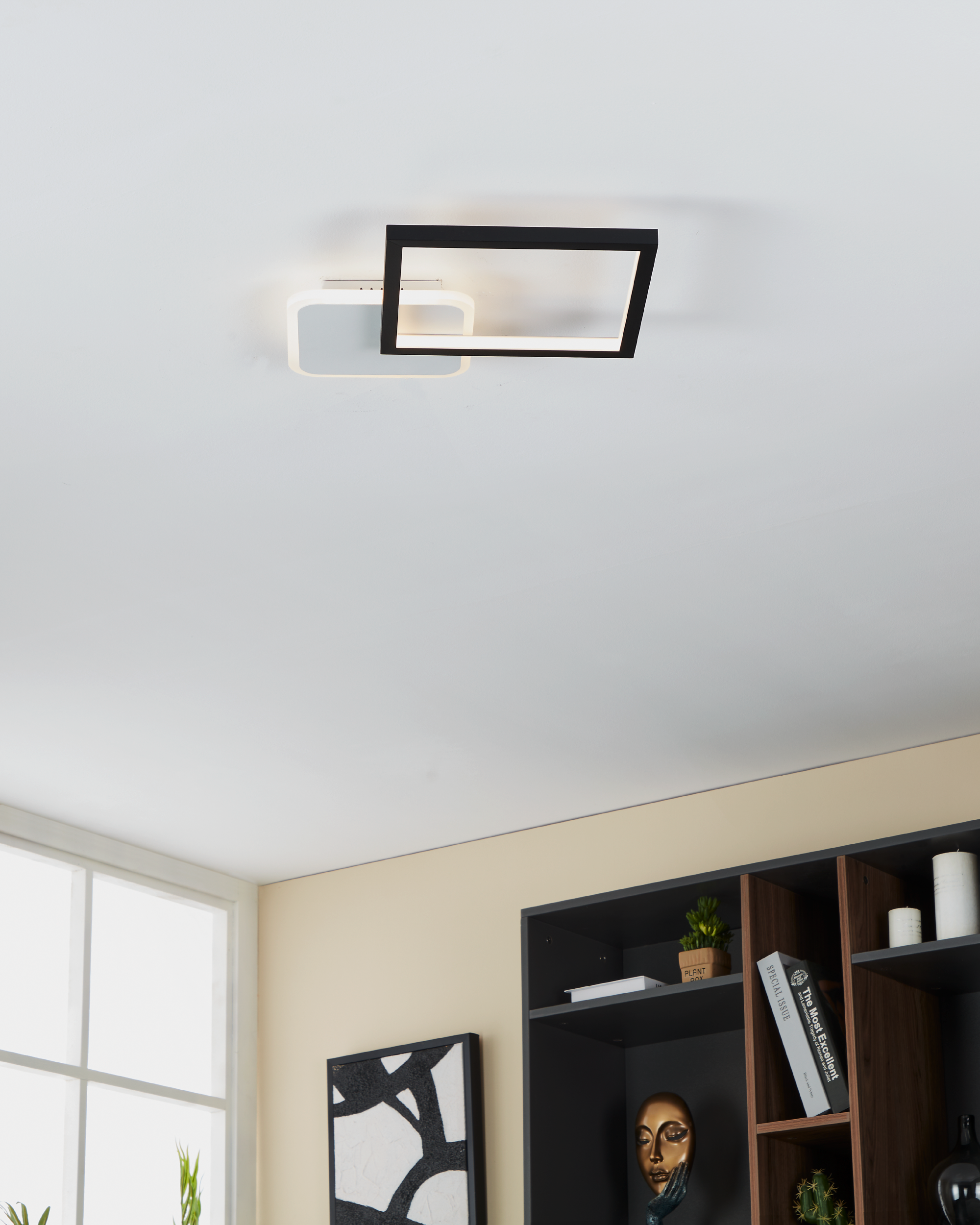 Eine moderne Deckenlampe mit zwei Quadraten und einem Rechteck, schwarz und weiß. Im Hintergrund ist ein Regal.