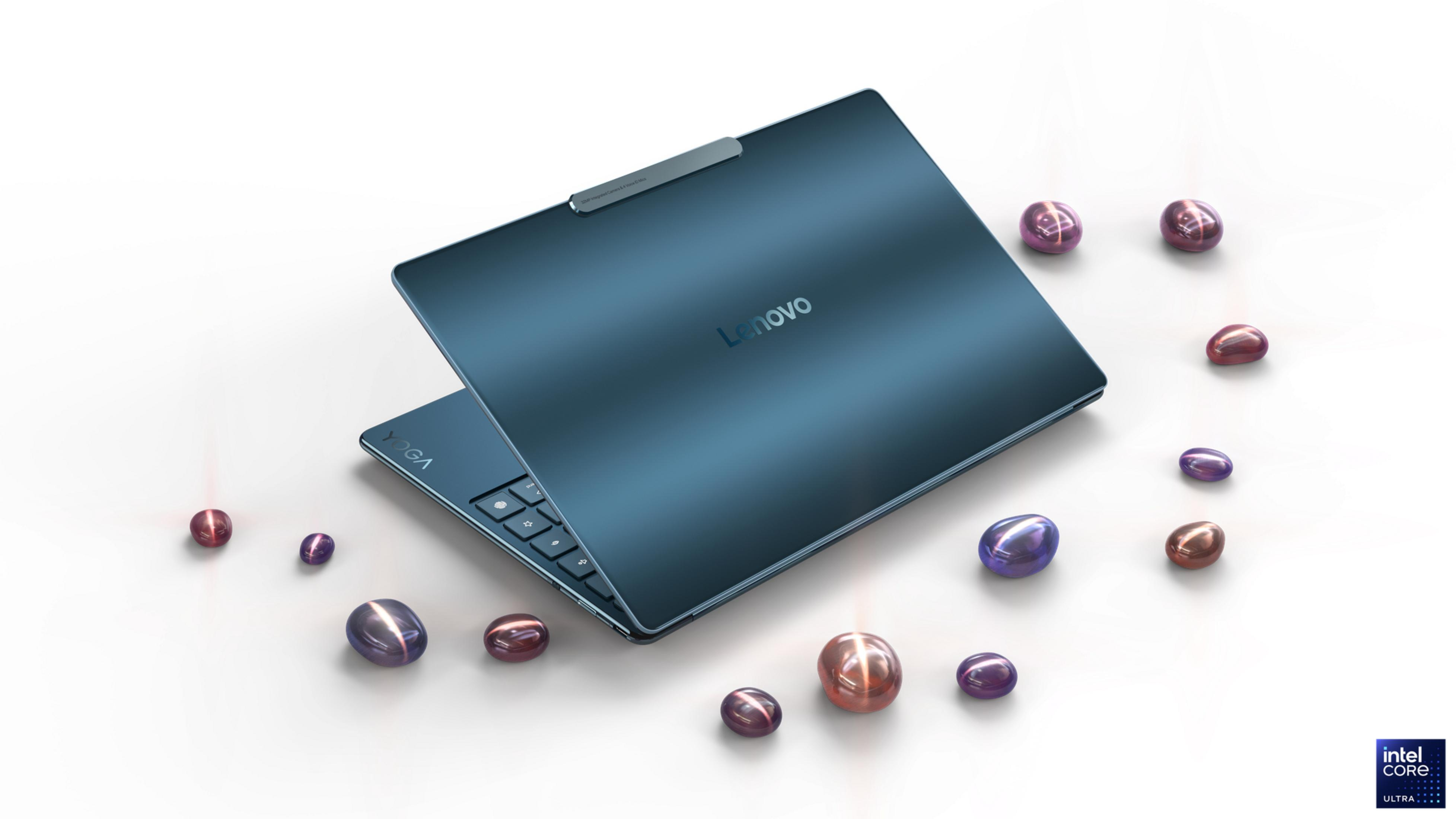 Niebieski laptop Lenovo Yoga, częściowo otwarty, otoczony obiektami przypominającymi klejnoty na białej powierzchni. Logo Intel Core Ultra.