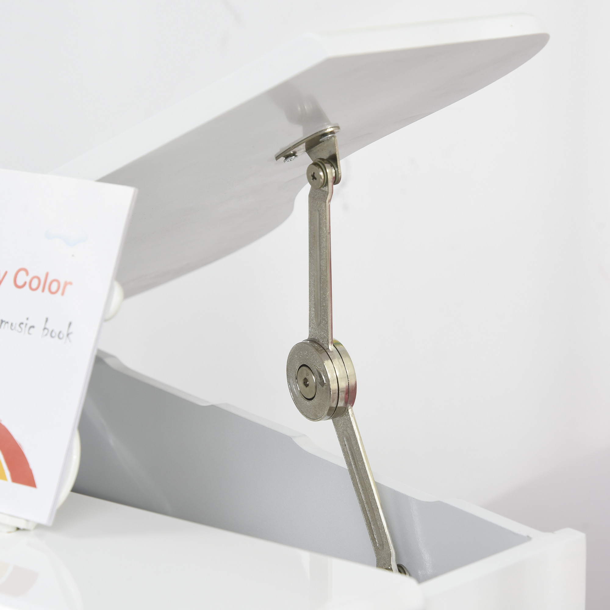 Caja de juguetes blanca con tapa abierta. Se ve una bisagra metálica. Hay un libro colorido dentro de la caja.