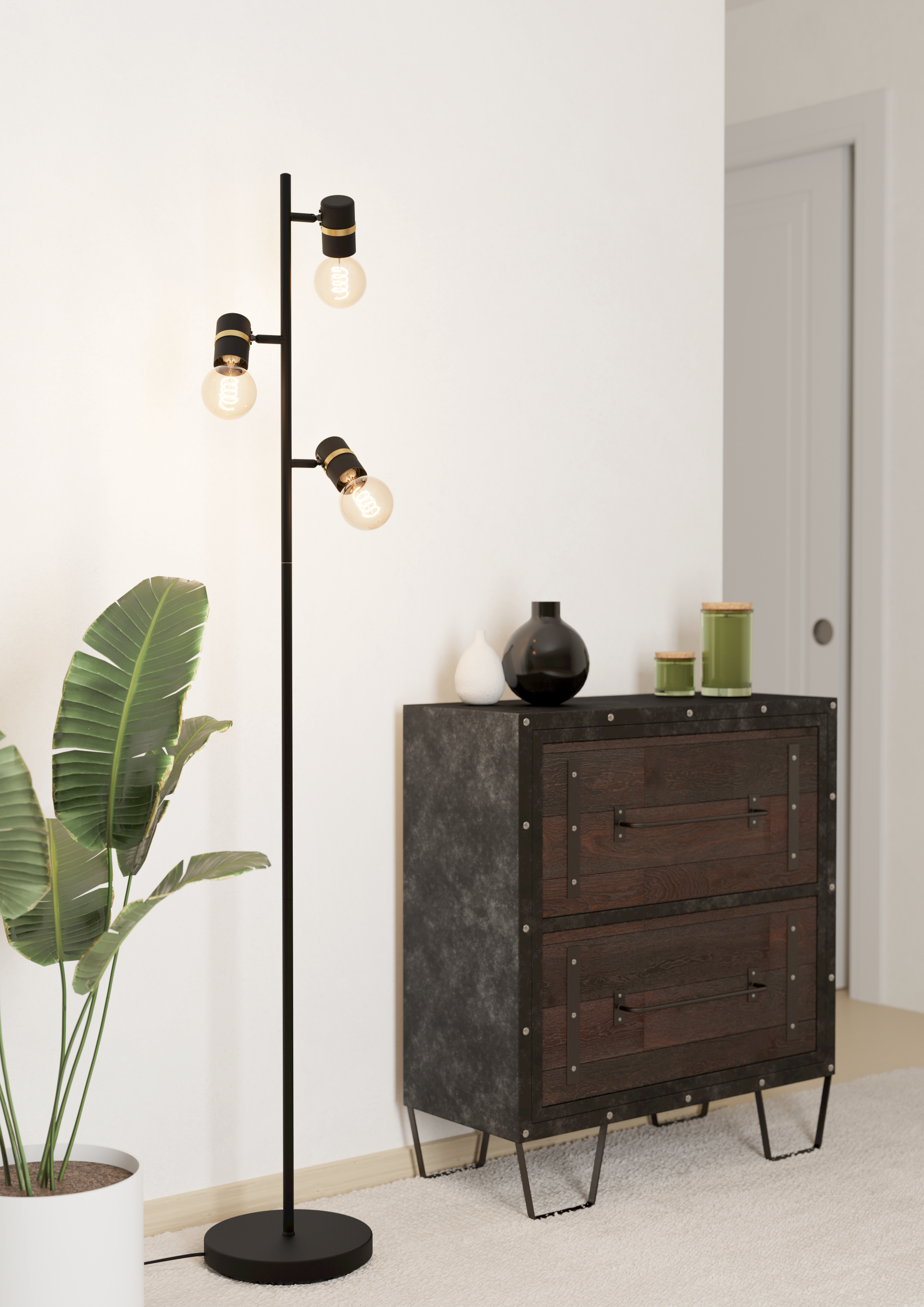 Zimmerecke mit Stehlampe, Kommode und Topfpflanze. Die Lampe hat drei leuchtende Glühbirnen.