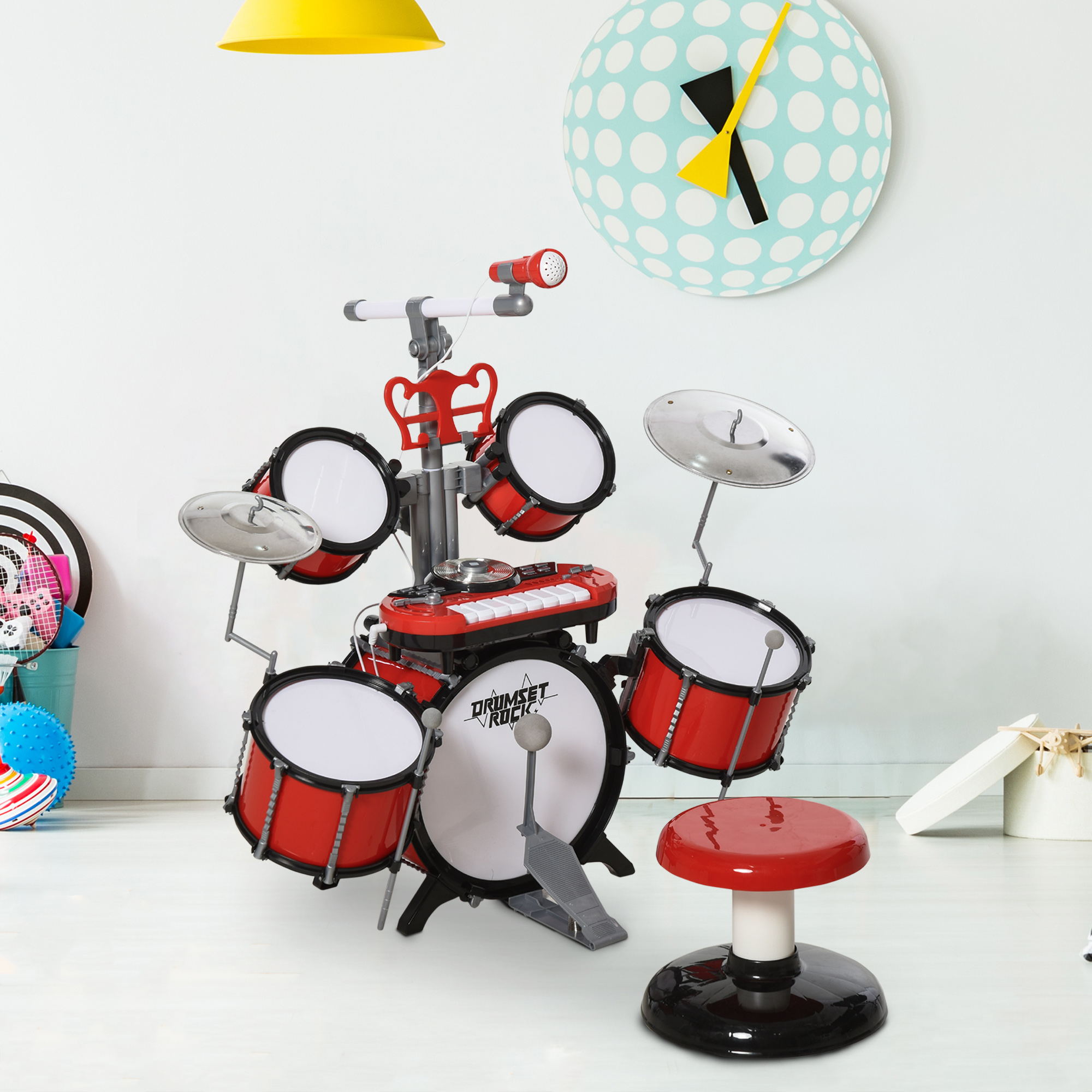 Un juego de batería de juguete con tambores rojos, platillos y un taburete está en una habitación. También se ven un reloj, una lámpara y algunos juguetes.