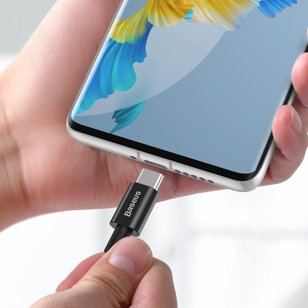 Ręka trzyma telefon z kolorowym ekranem. Czarny kabel USB-C Baseus jest podłączony do telefonu.