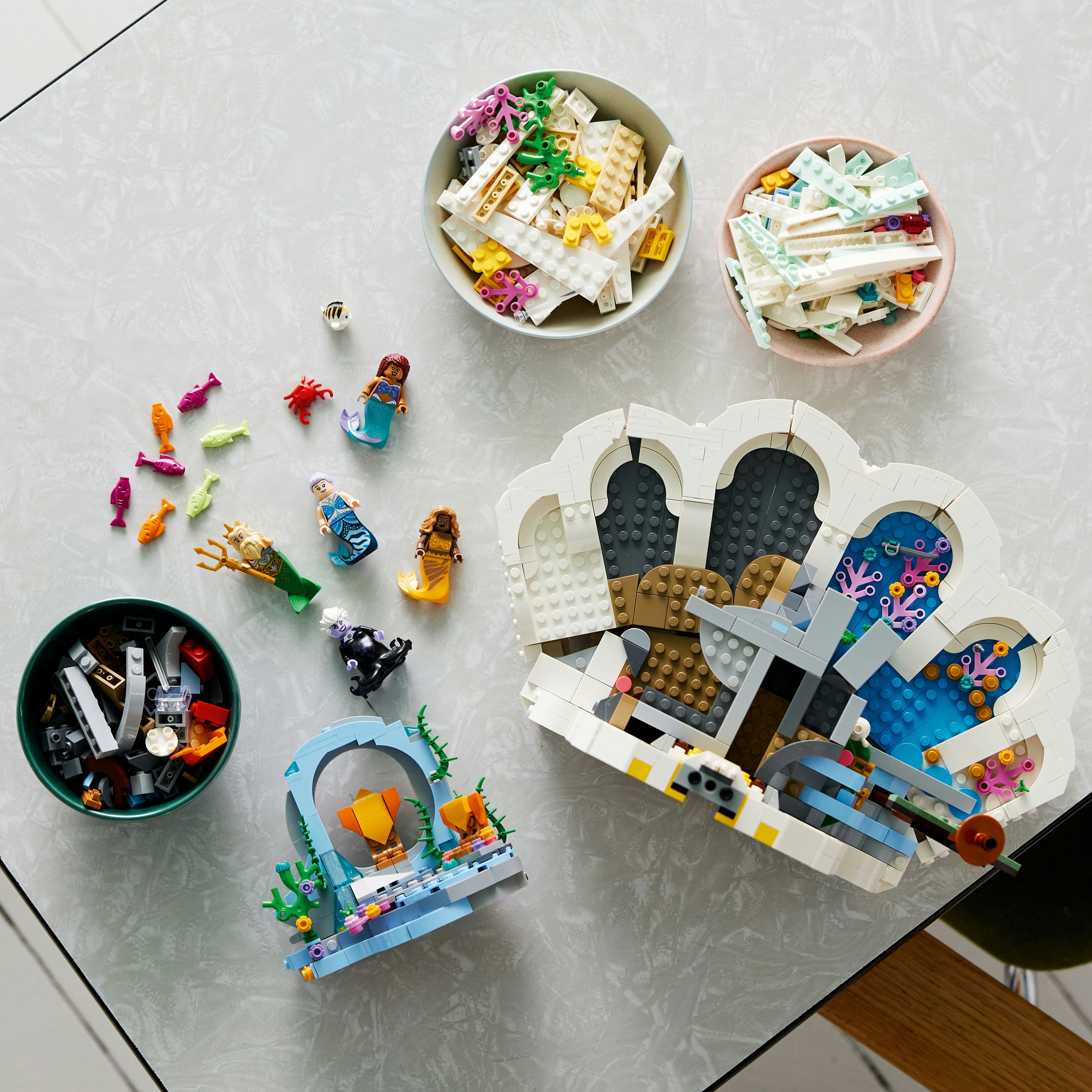 Bovenaanzicht van Lego-onderdelen, bakjes met stenen, zeemeerminfiguren en een schelpstructuur.