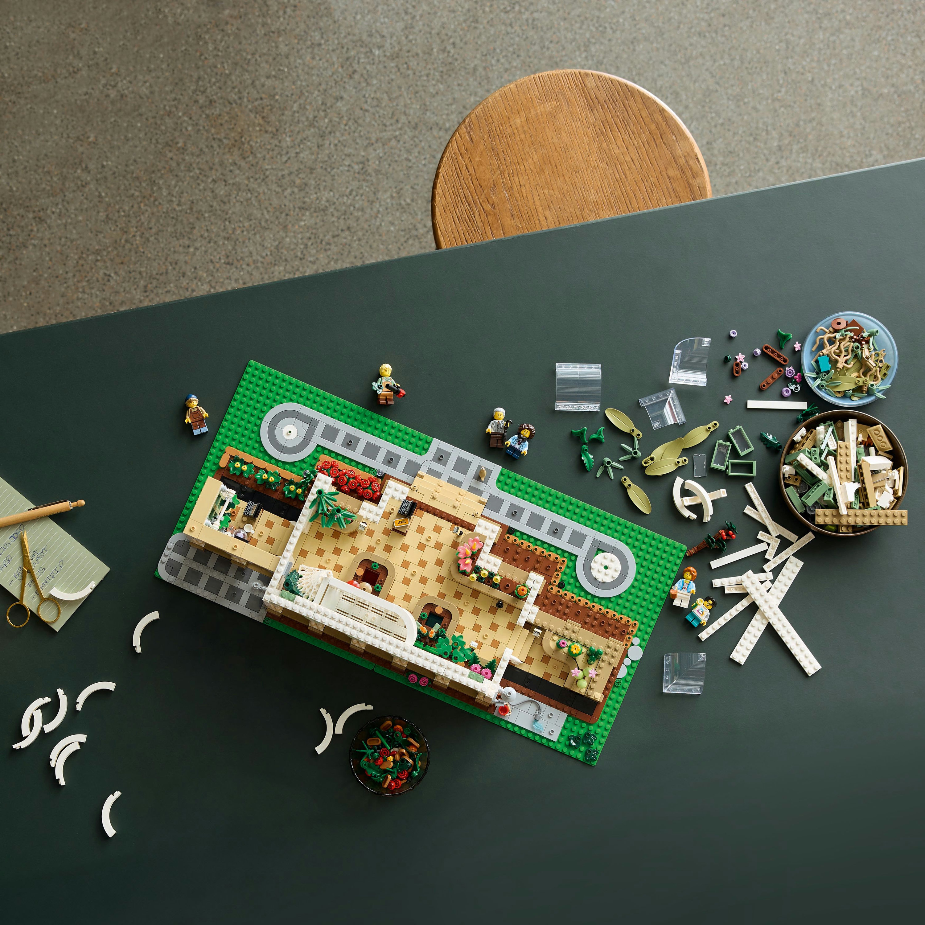 Widok z góry na stół z klockami Lego i minifigurkami. Widoczna jest częściowo zbudowana konstrukcja Lego.