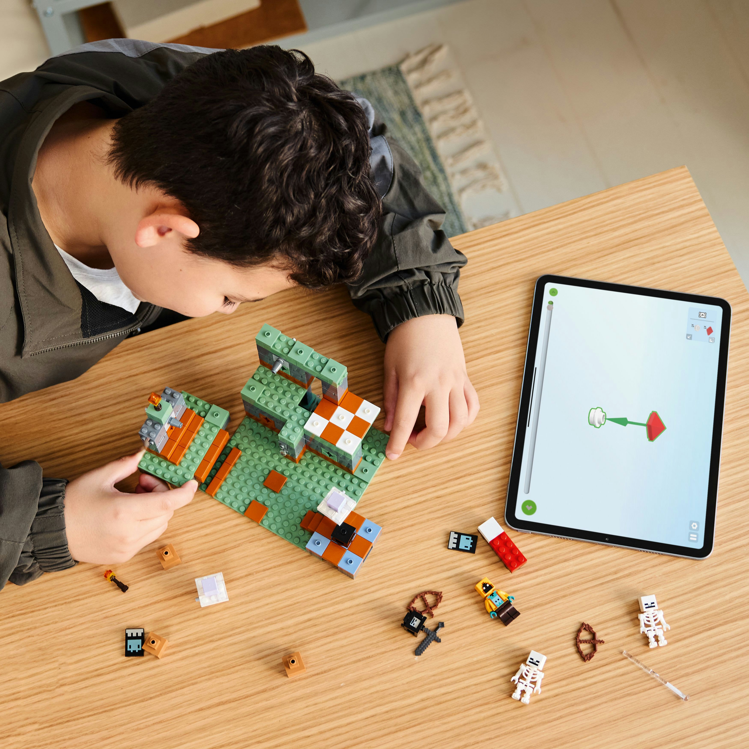 Dziecko buduje zestaw Lego Minecraft na drewnianym stole z tabletem pokazującym instrukcje.