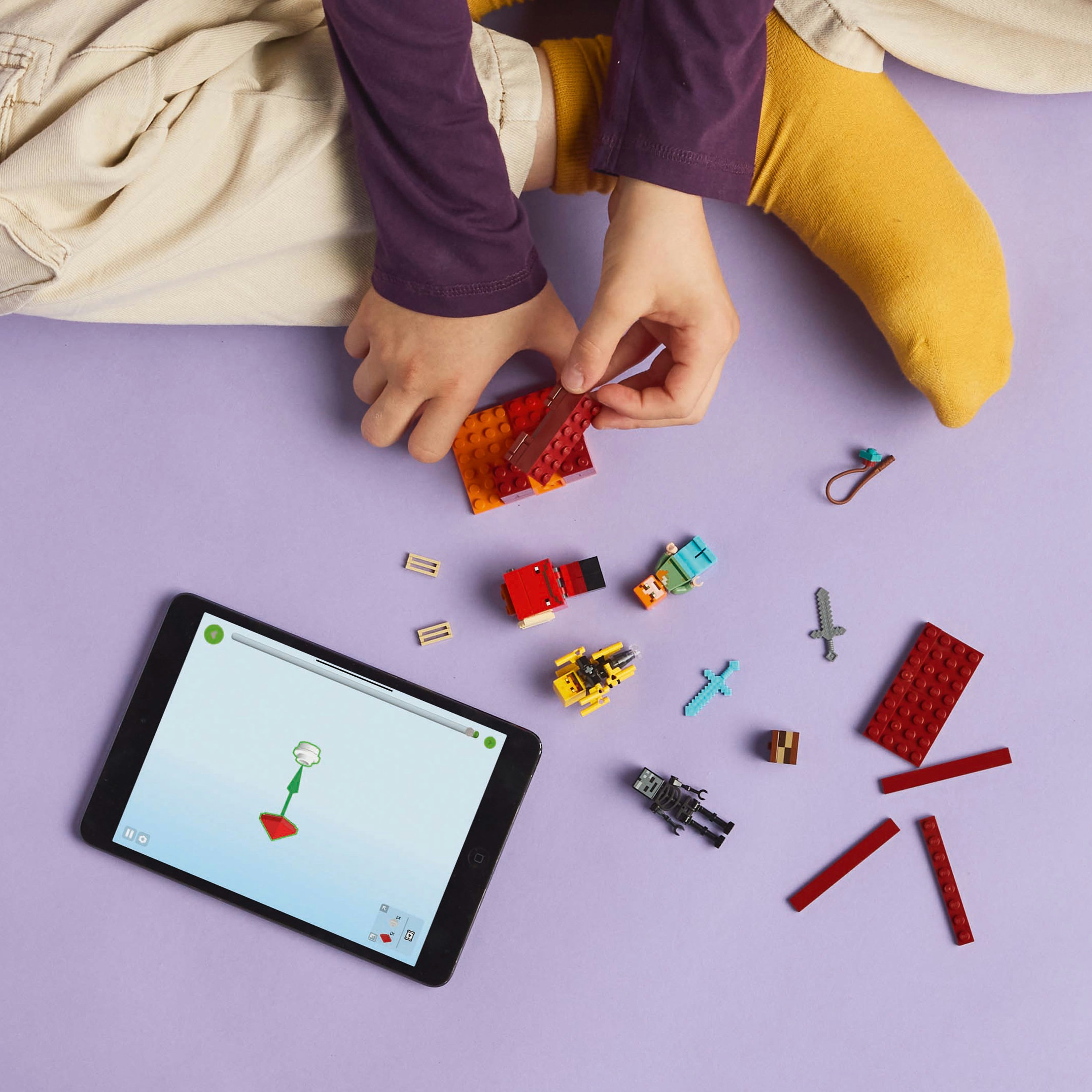 Ręce składające zestaw LEGO z figurkami, tablet z instrukcjami i inne elementy na fioletowej powierzchni.