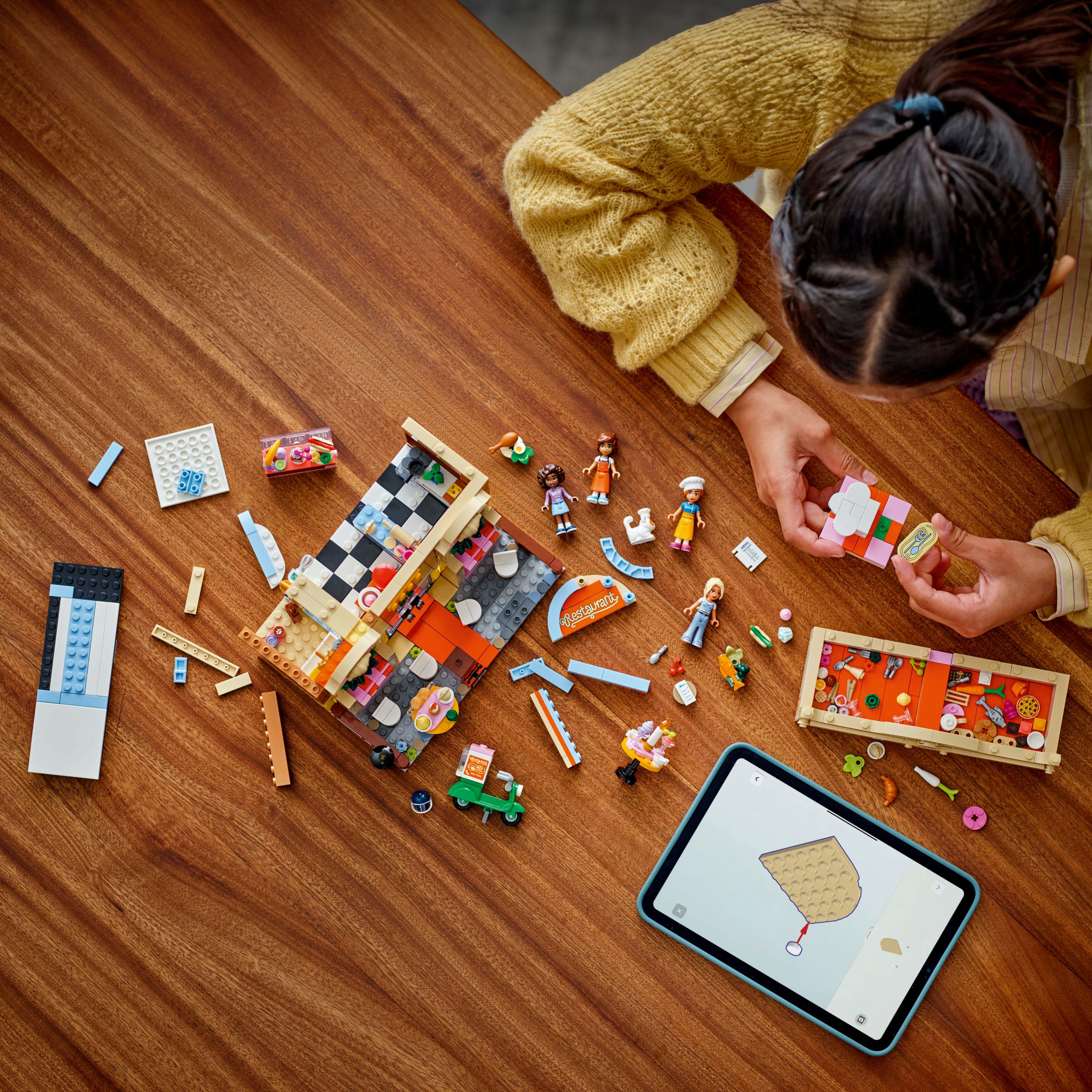 Osoba buduje zestaw Lego na drewnianym stole. Różne klocki i figurki Lego są rozrzucone.