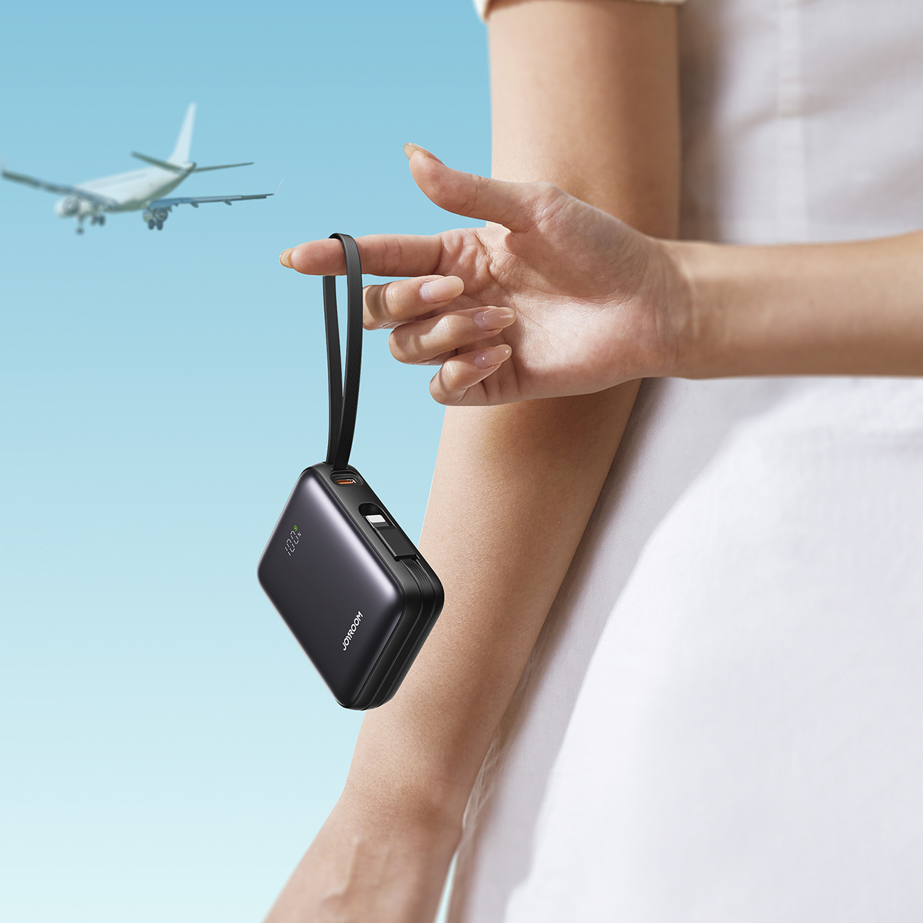 Ręka trzyma czarny power bank z samolotem w tle.