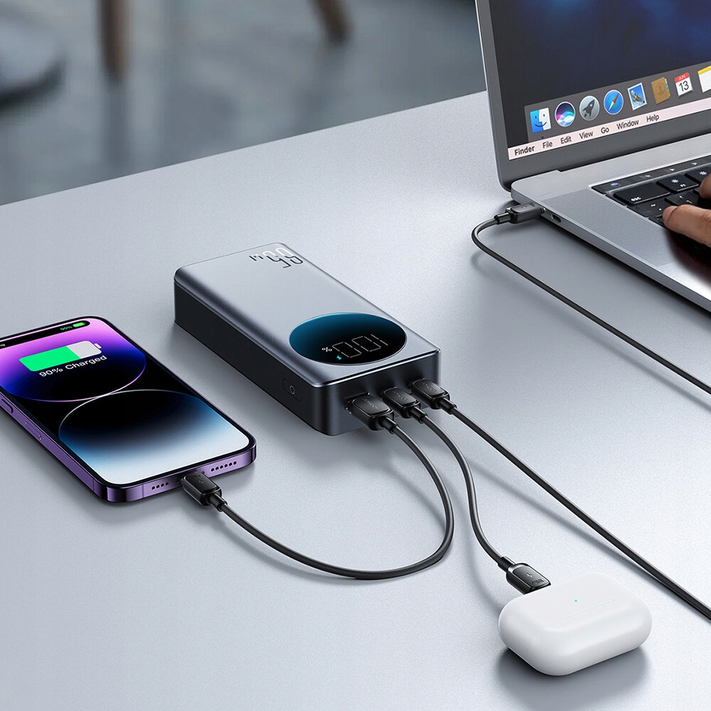 Power bank ładujący wiele urządzeń: telefon, laptop i słuchawki. Power bank pokazuje 100% naładowania.