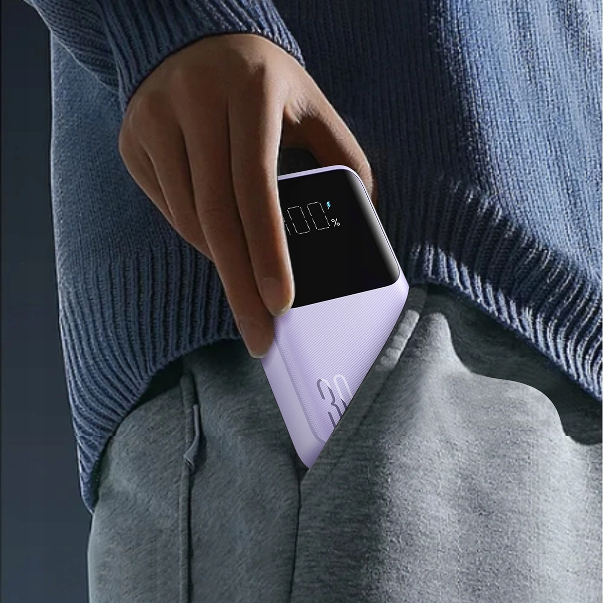 Ręka osoby i power bank. Power bank jest fioletowy i w kieszeni.